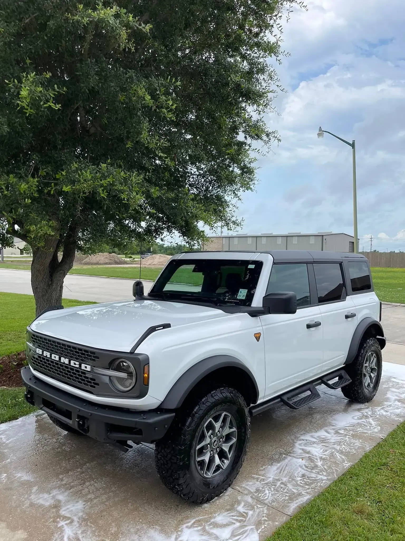 White Ford Bronco parked on a driveway with suds. Black accents, under a tree.