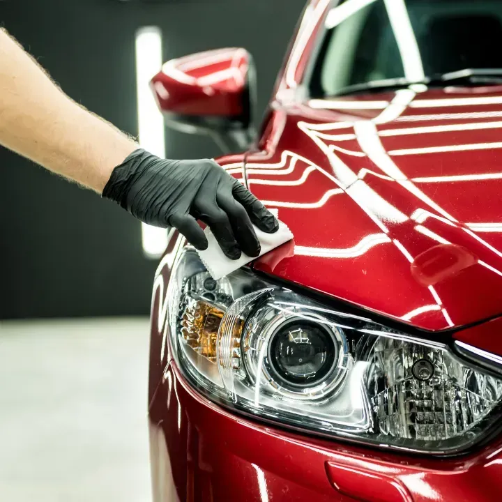 Hand in black glove polishing a red car's hood with a white applicator.