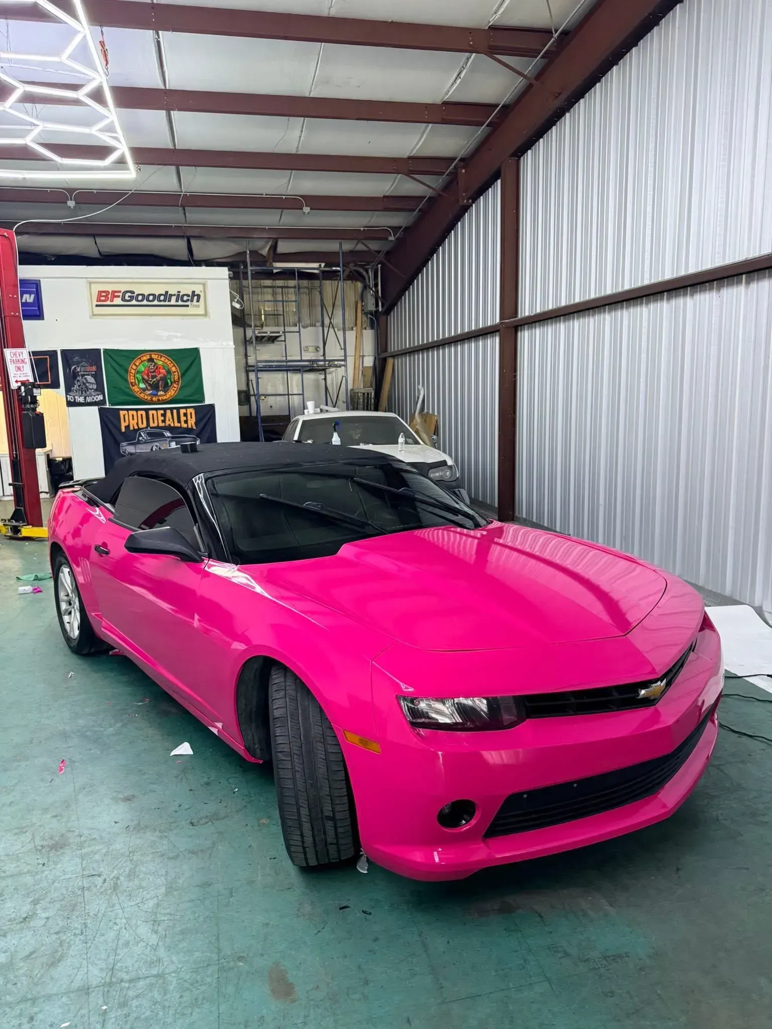 A bright pink Chevrolet Camaro convertible inside a garage.