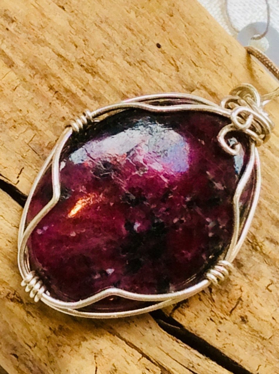 Jewelry and gemstones scattered on a wooden table, including necklaces, rings, and pendants in various colors.