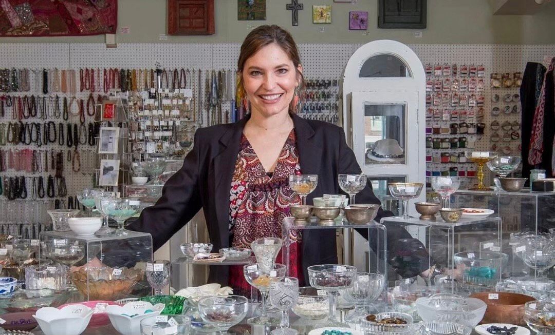 Woman standing behind a display of glassware in a shop, smiling.