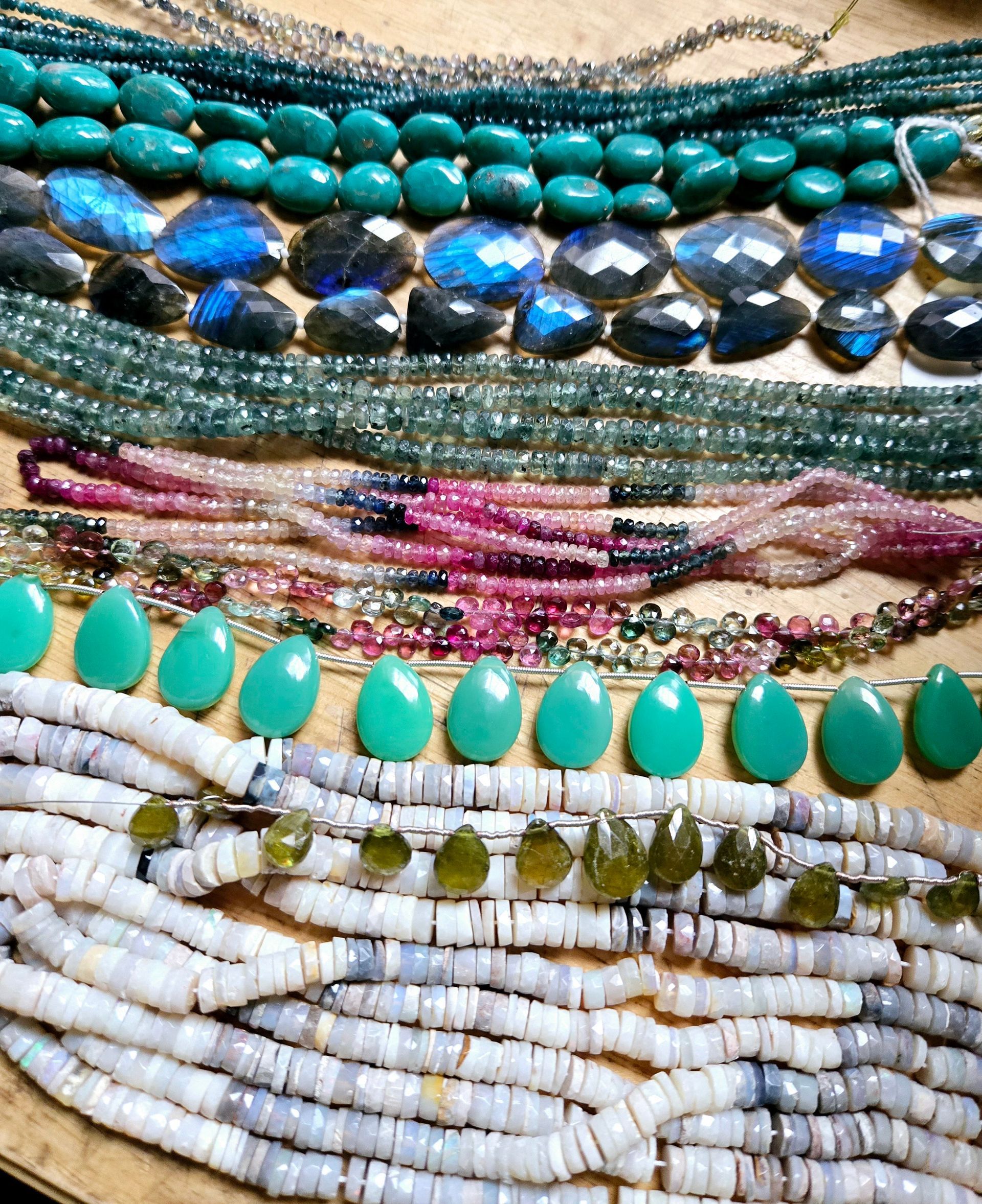 A wooden table displays jewelry-making tools and beads, with jars and a wooden box.