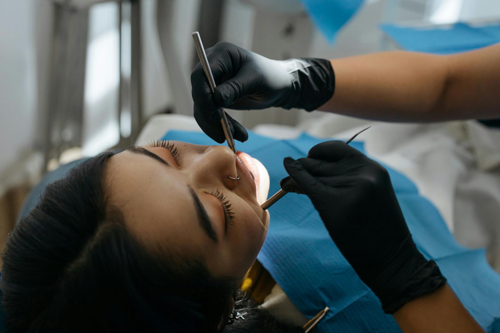 Dentista examinando los dientes de un paciente. El paciente está acostado en una silla; el dentista usa guantes negros y sostiene las herramientas.