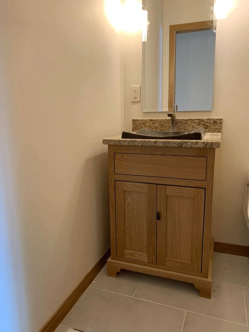 A bathroom with a wooden vanity , sink , mirror and toilet.
