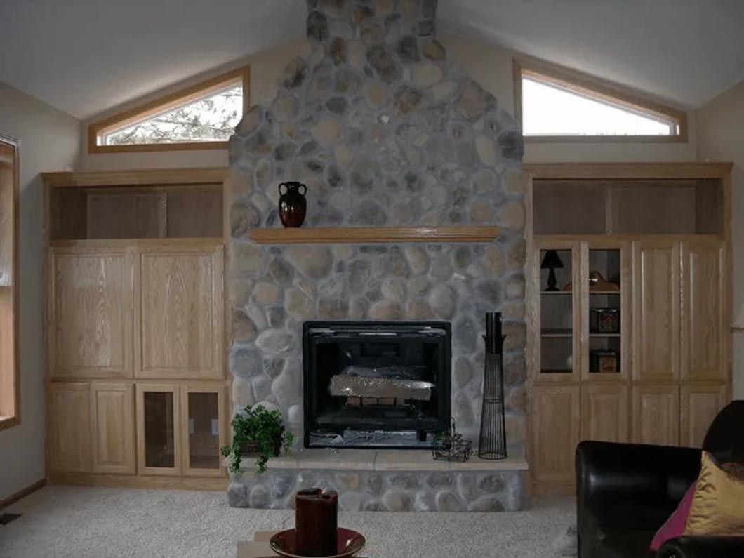 A living room with a stone fireplace and built in cabinets