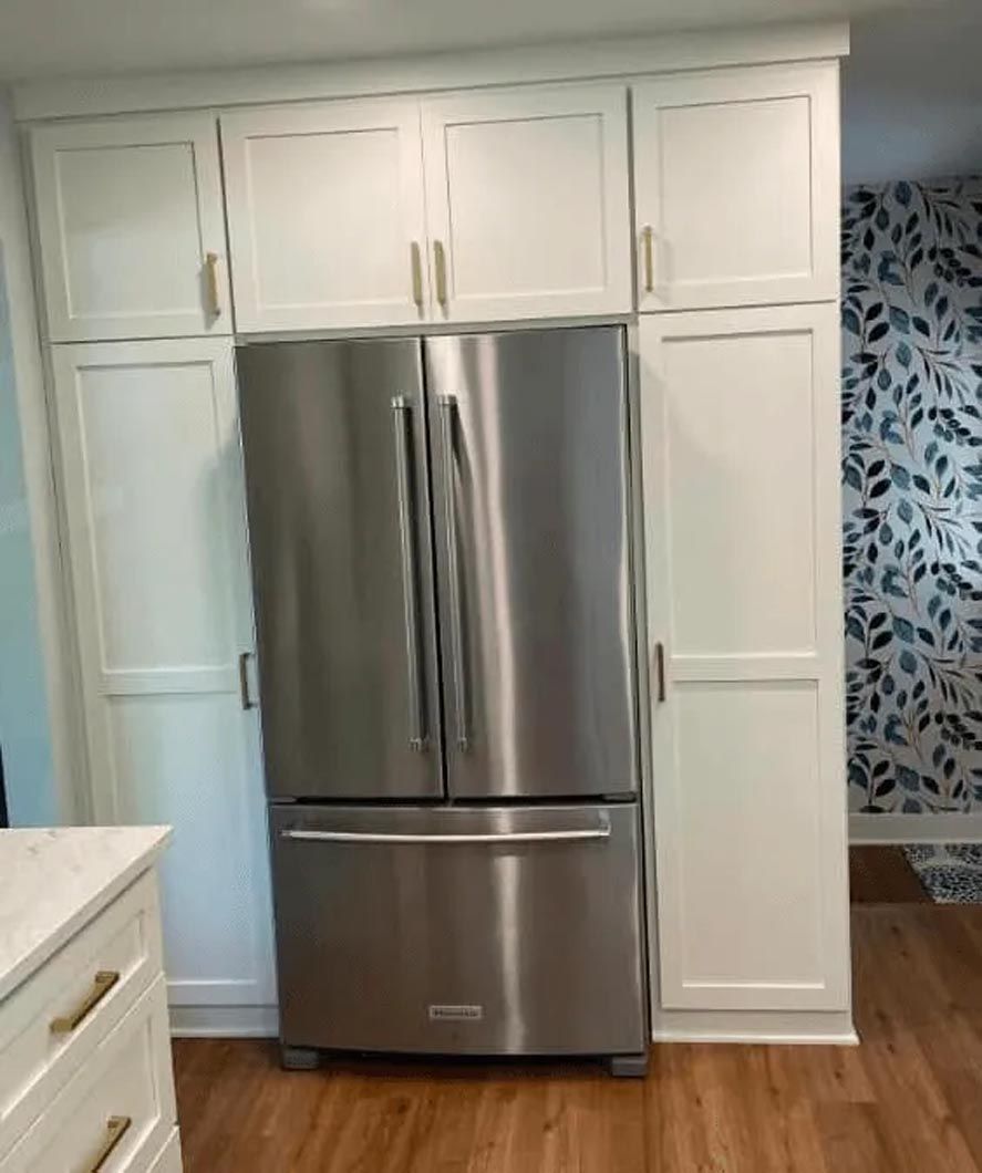 A stainless steel refrigerator is surrounded by white cabinets in a kitchen.