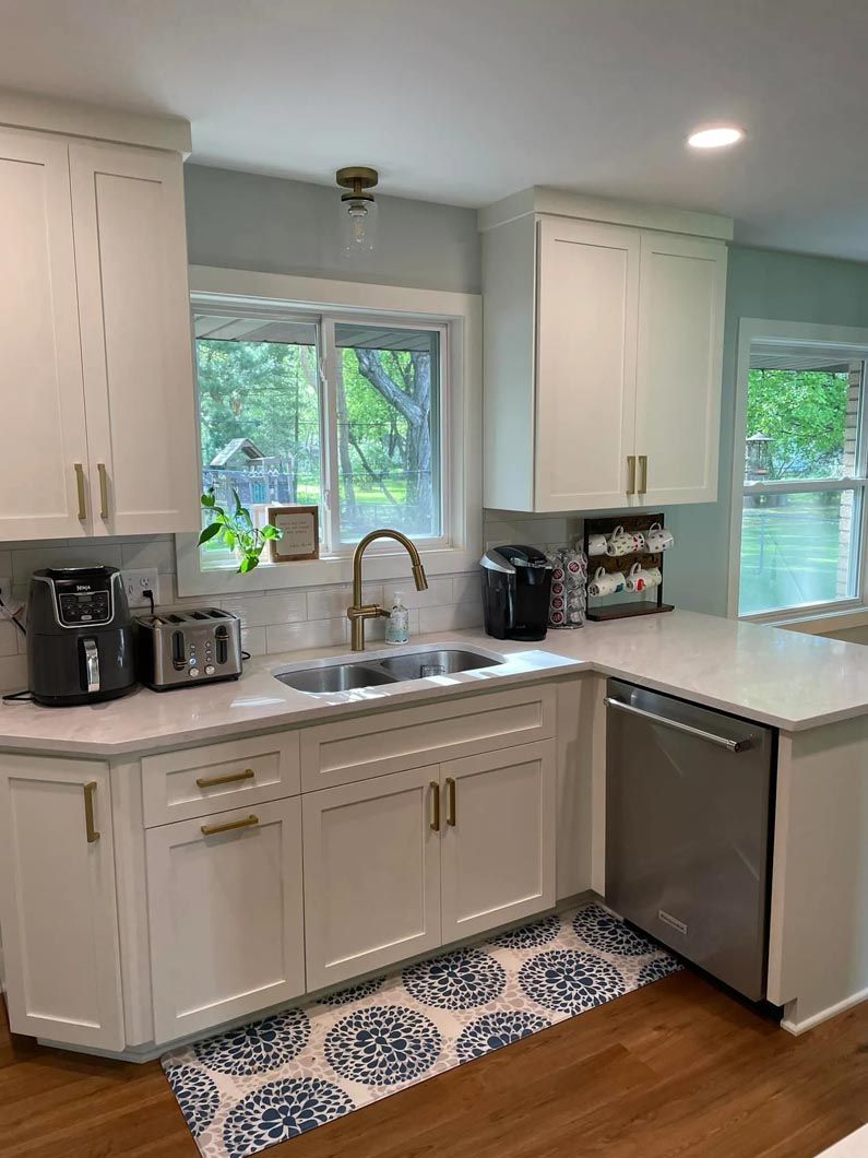 A kitchen with white cabinets , a sink , a dishwasher and a window.