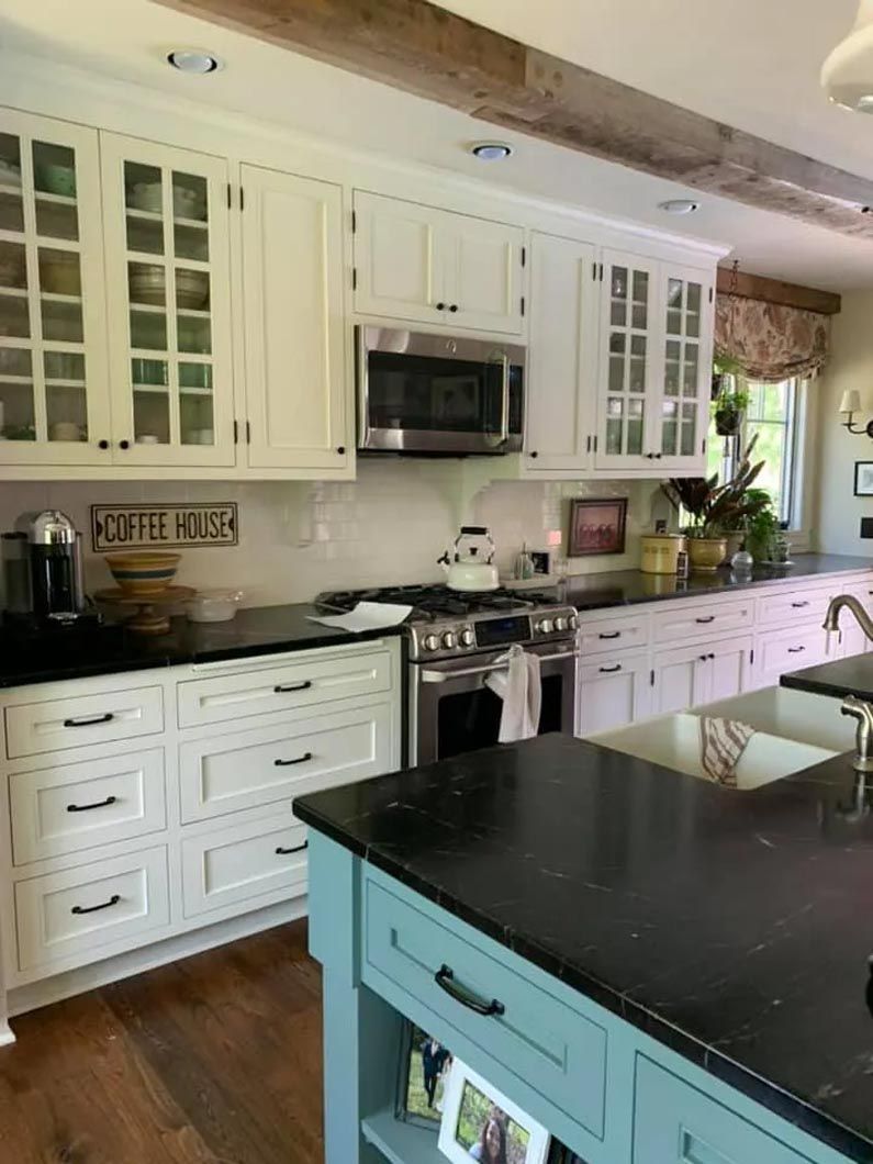 A kitchen with white cabinets , black counter tops , and a blue island.