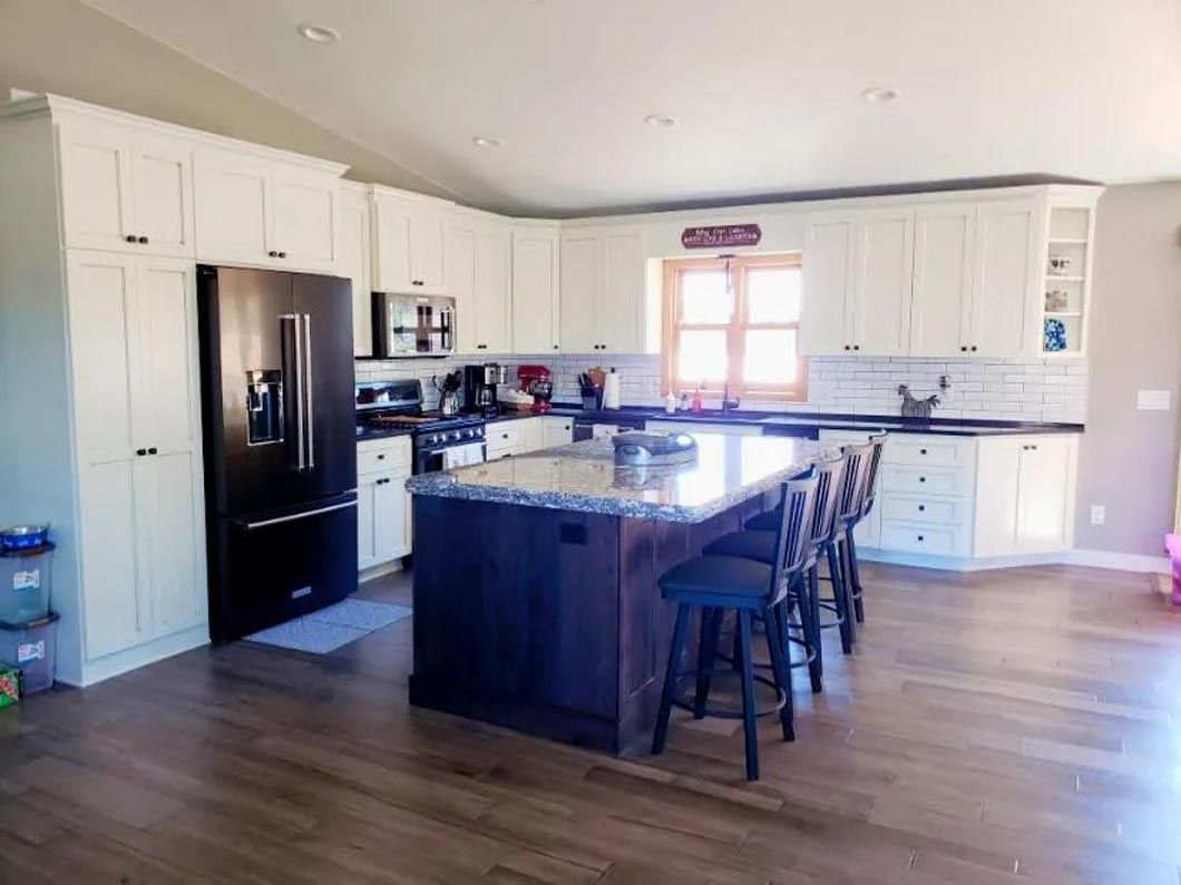 A kitchen with white cabinets , a black refrigerator , and a large island.