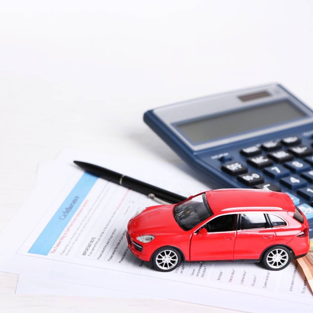 A red toy car is sitting on a piece of paper next to a calculator and pen.