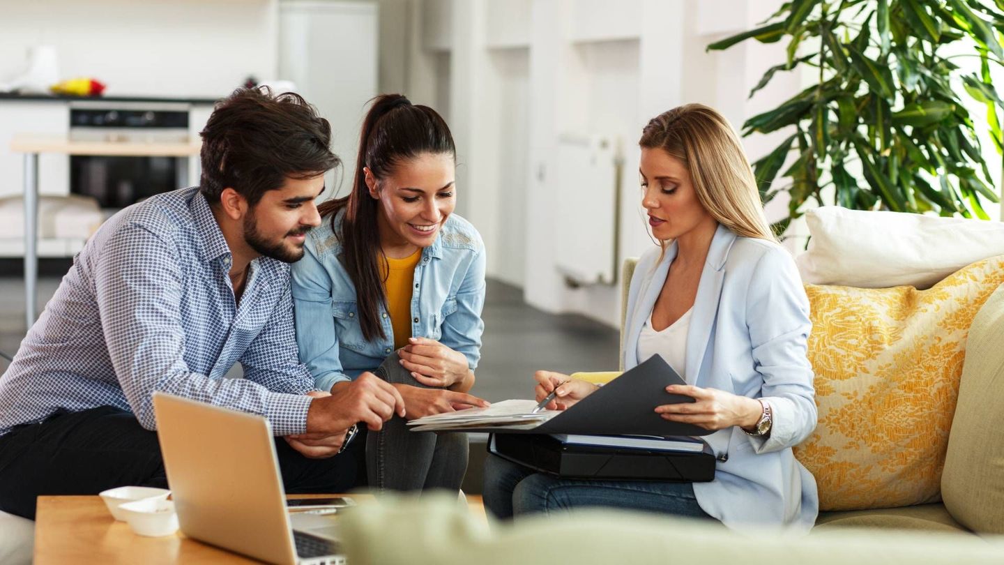 A man and a woman are sitting on a couch talking to a real estate agent.