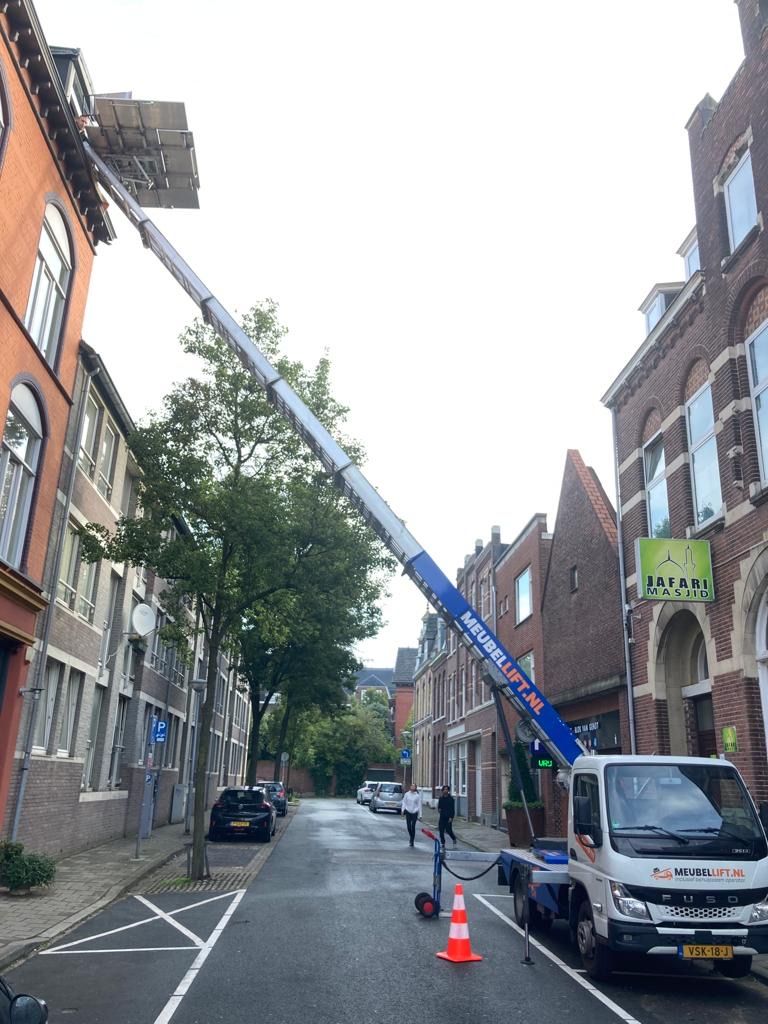 Een kraan staat aan de kant van de straat, voor een gebouw.