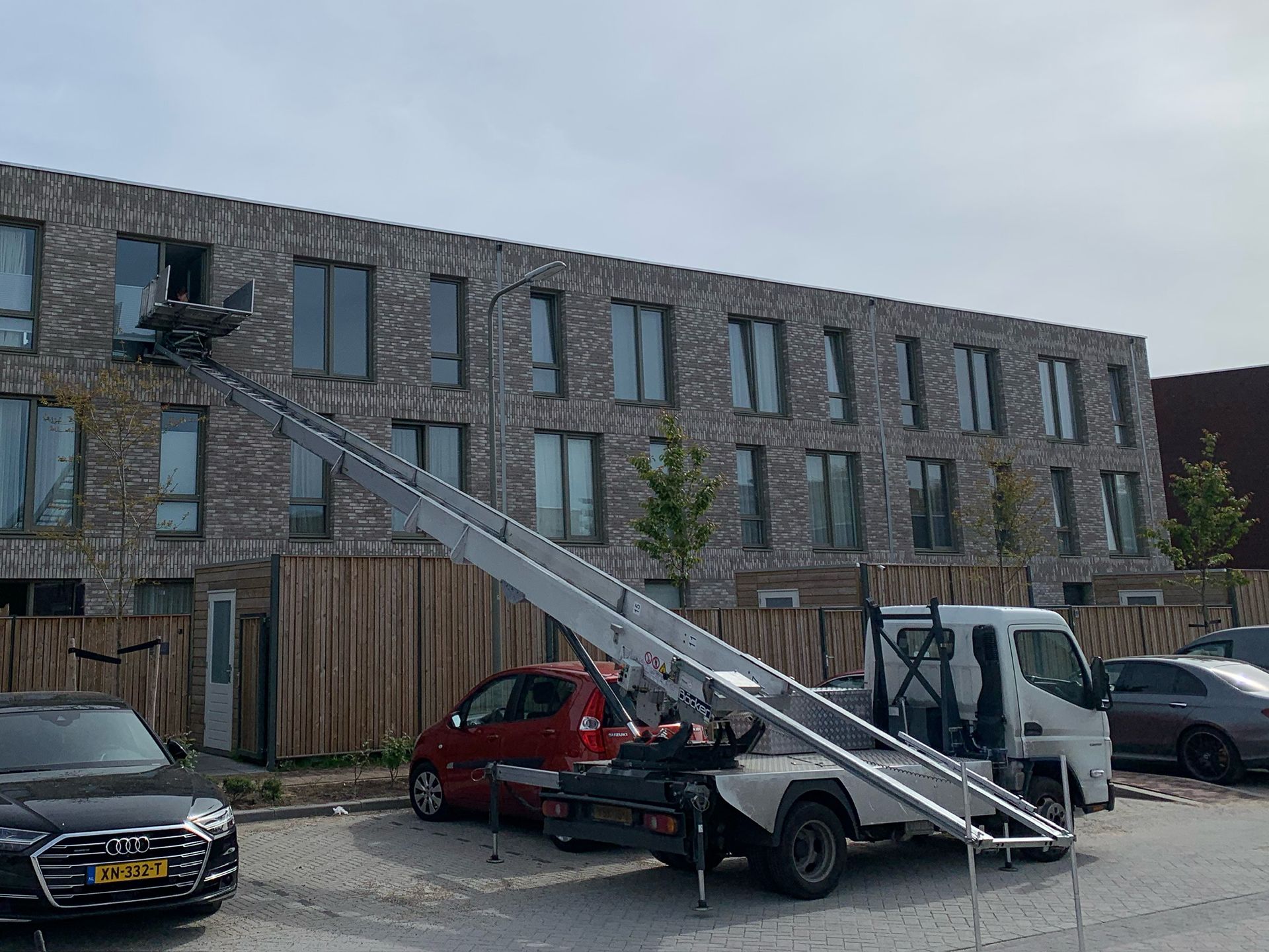 Een vrachtwagen met daaraan een ladder staat geparkeerd voor een bakstenen gebouw.