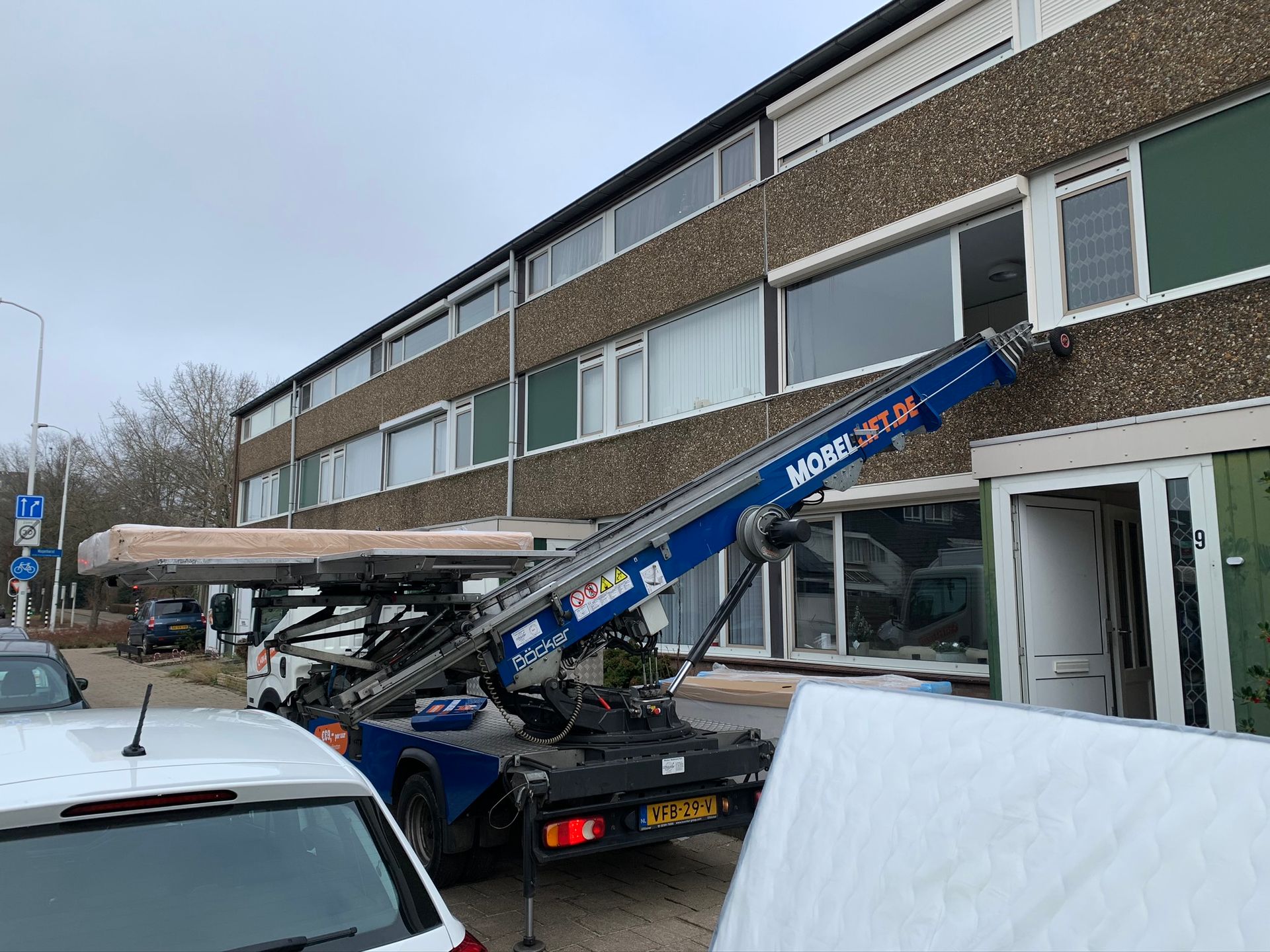 Een vrachtwagen met daaraan een kraan staat voor een gebouw geparkeerd.