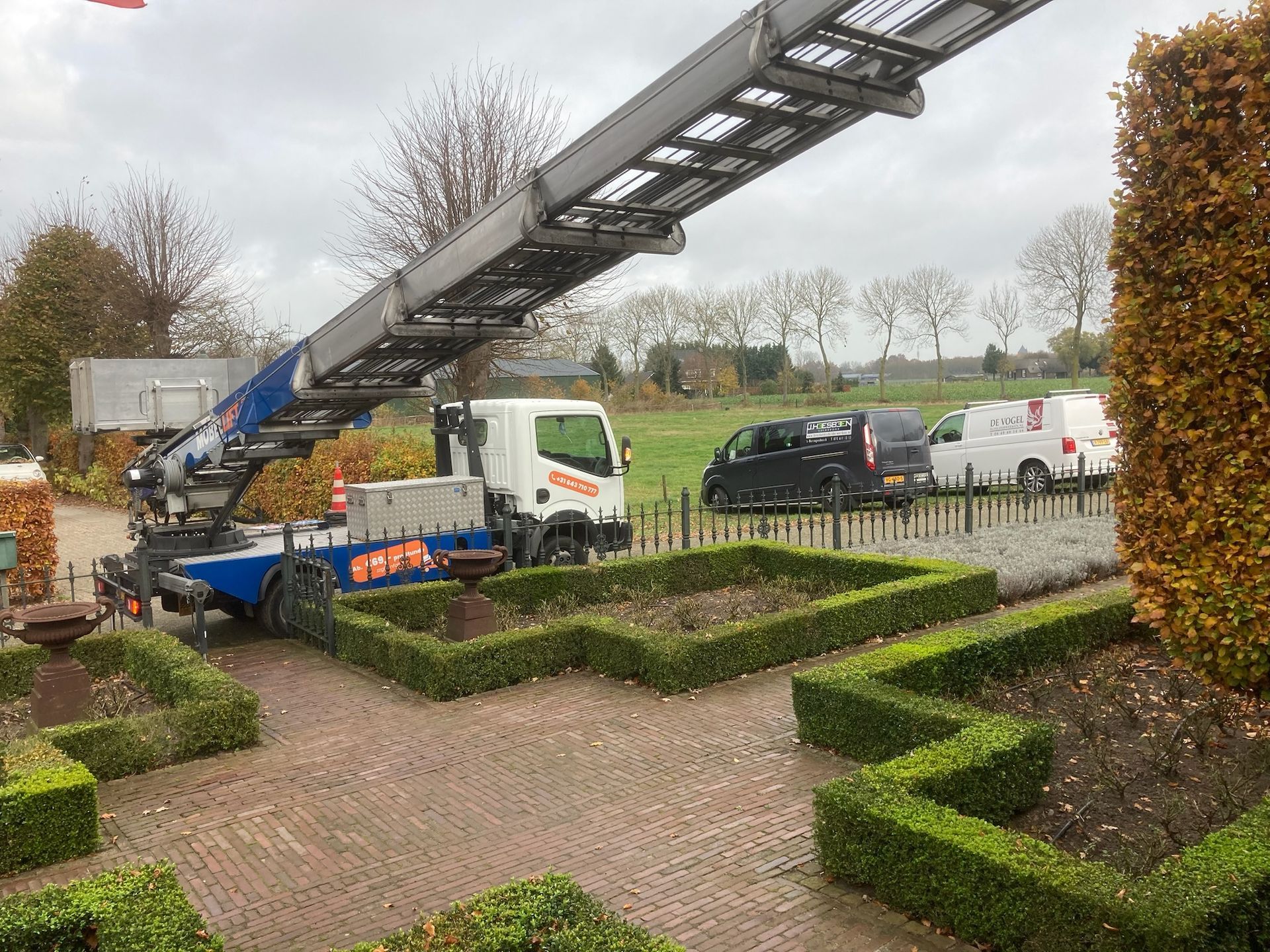 Een kraan staat bovenop een vrachtwagen in een tuin.