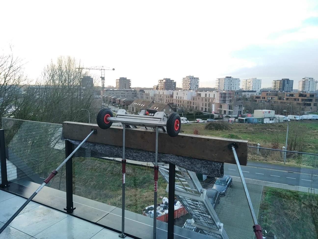 Een houten plank met wielen staat op een balkon met uitzicht op een stad.