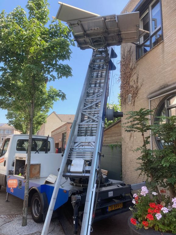 Een vrachtwagen met daaraan een ladder staat voor een gebouw geparkeerd.