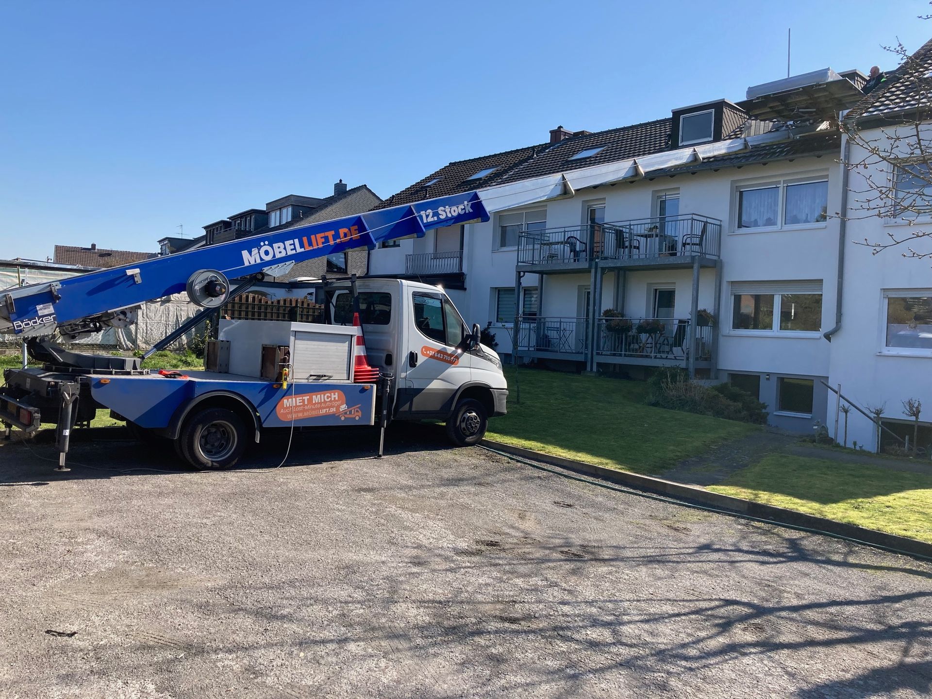 Een vrachtwagen met daarop een kraan staat geparkeerd voor een gebouw.