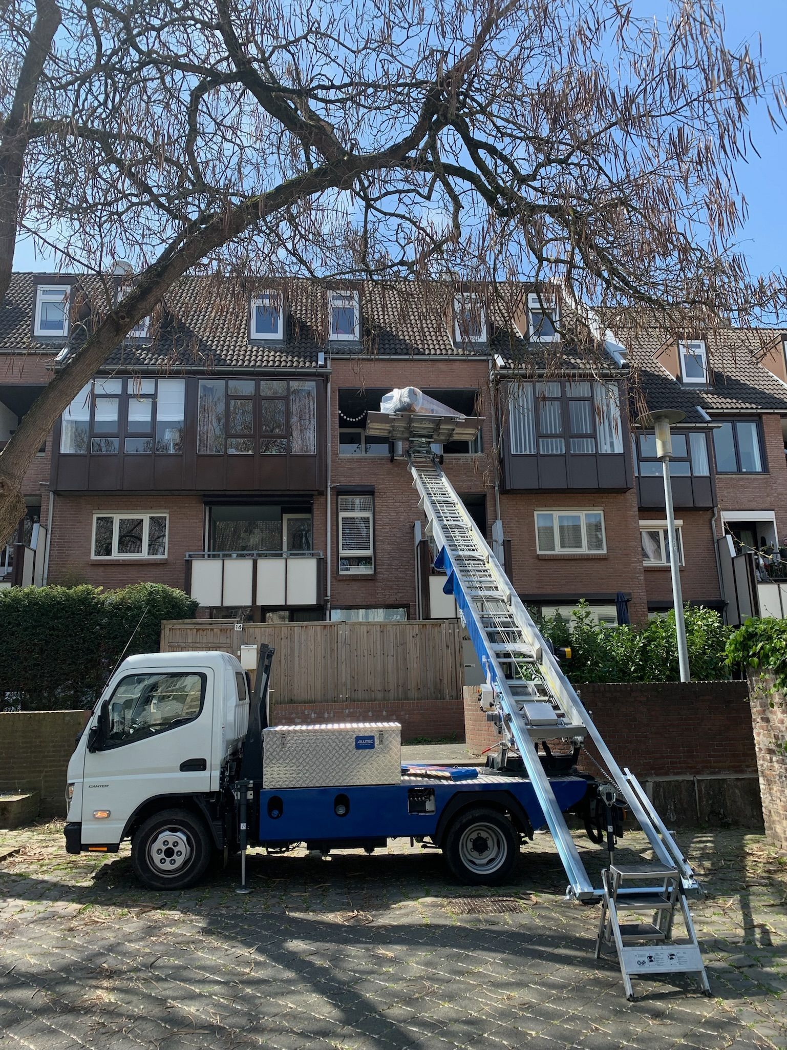 Een vrachtwagen met daaraan een ladder staat voor een gebouw geparkeerd.