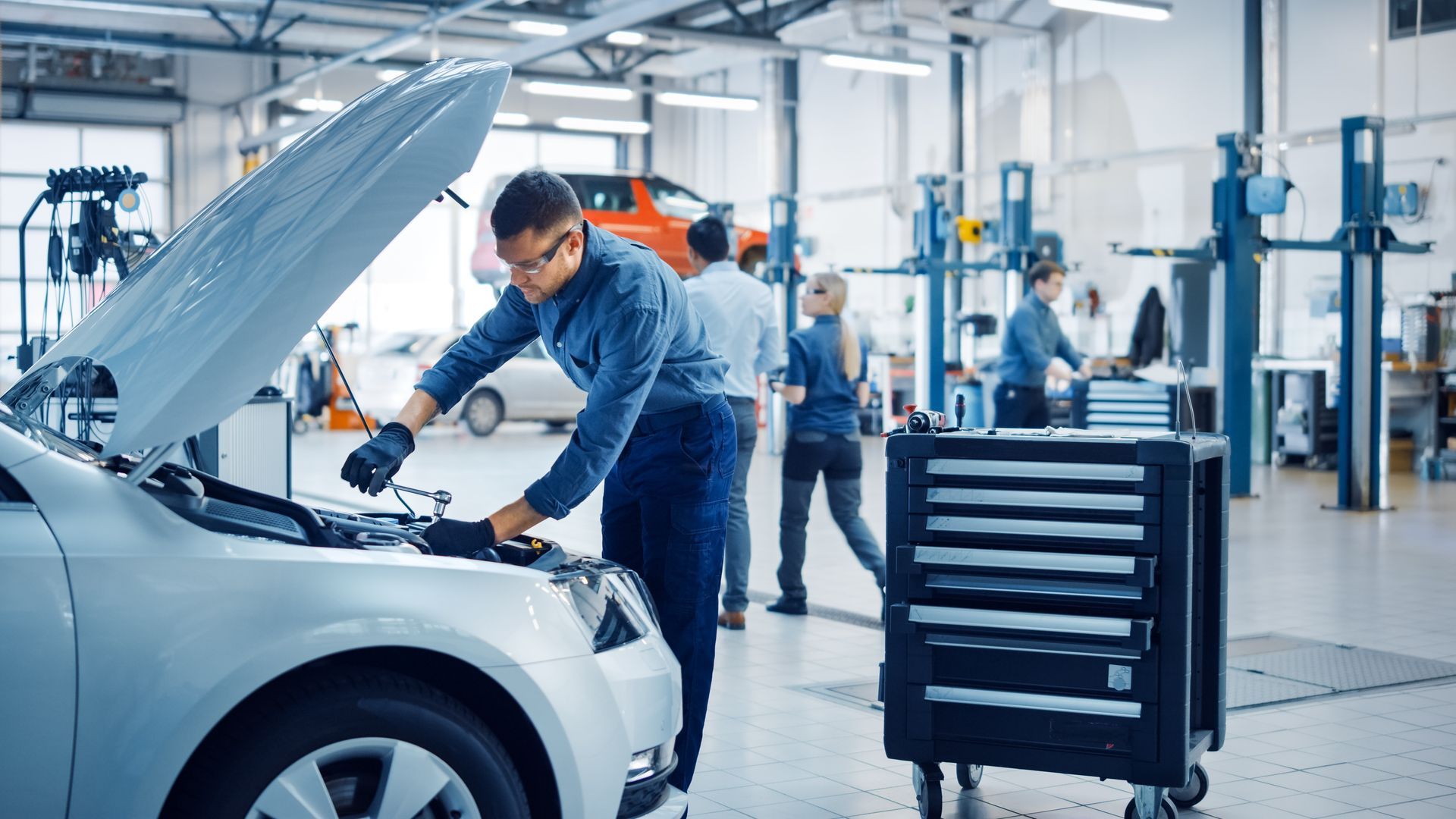 A mechanic performing maintenance under the hood of a car. A mechanic performing maintenance under the hood of a car.