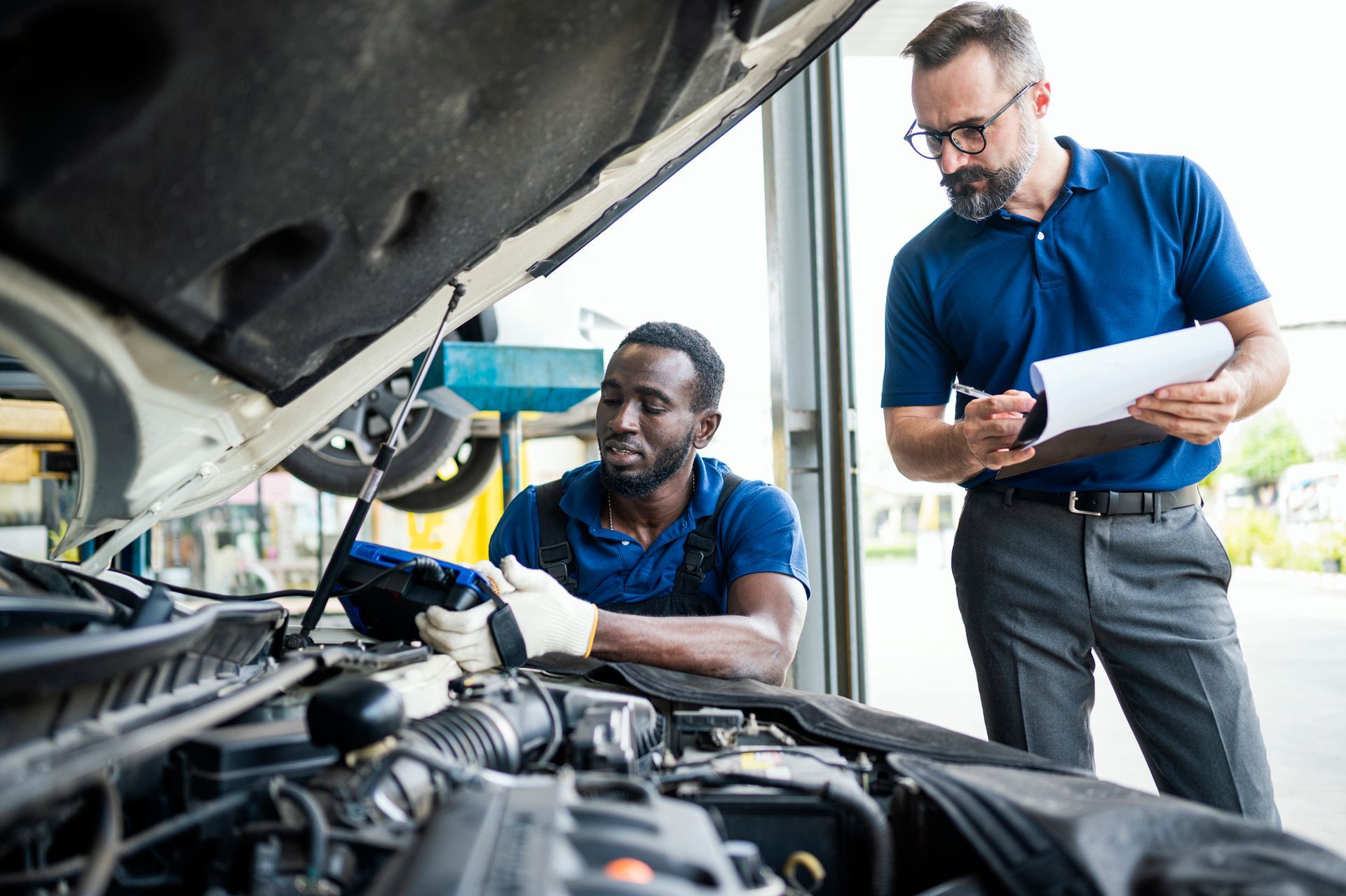 Technician and supervisor reviewing engine diagnostics during full-service auto repair at garage.