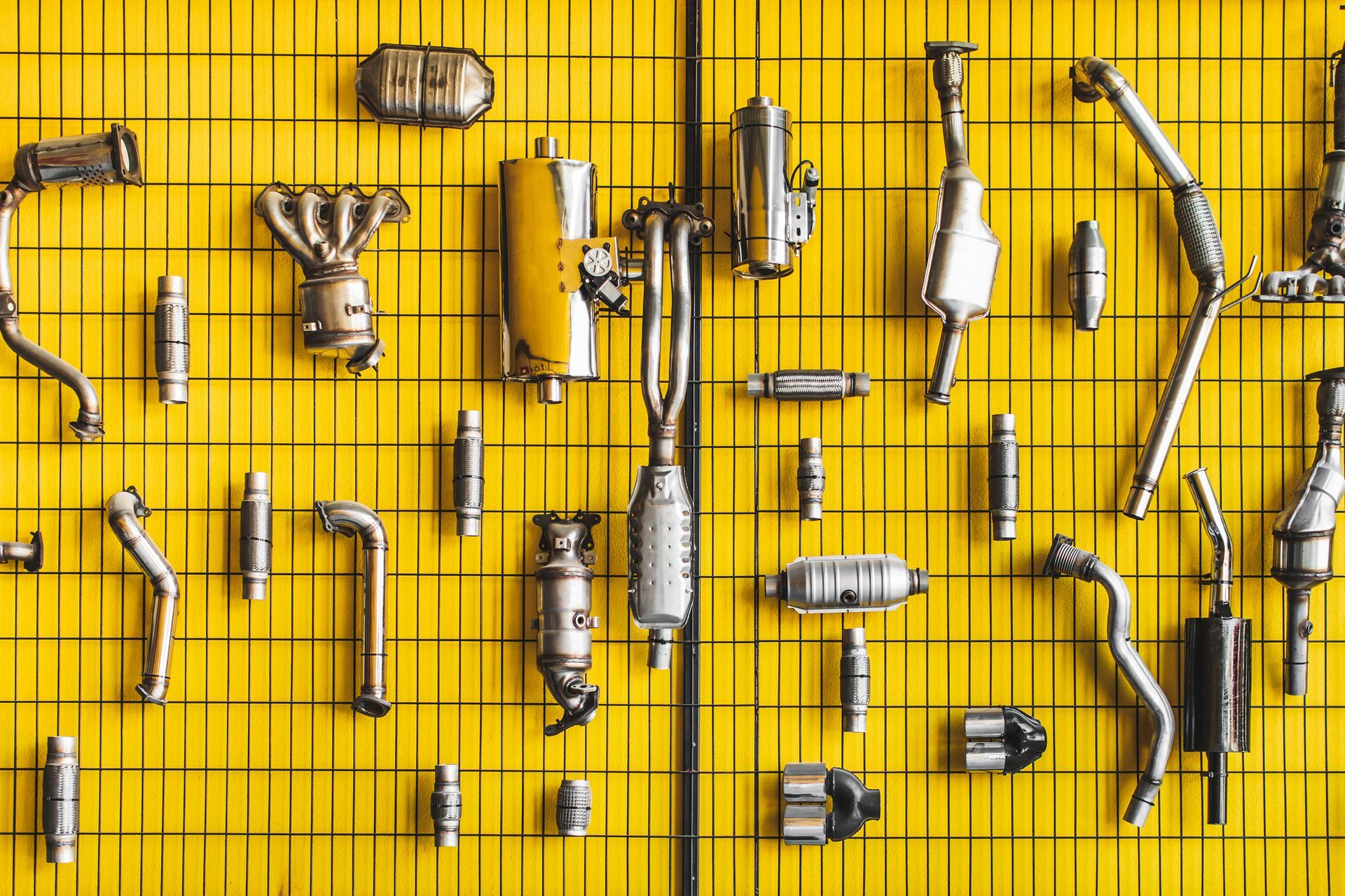 Car exhaust parts arranged neatly on a yellow grid backdrop.