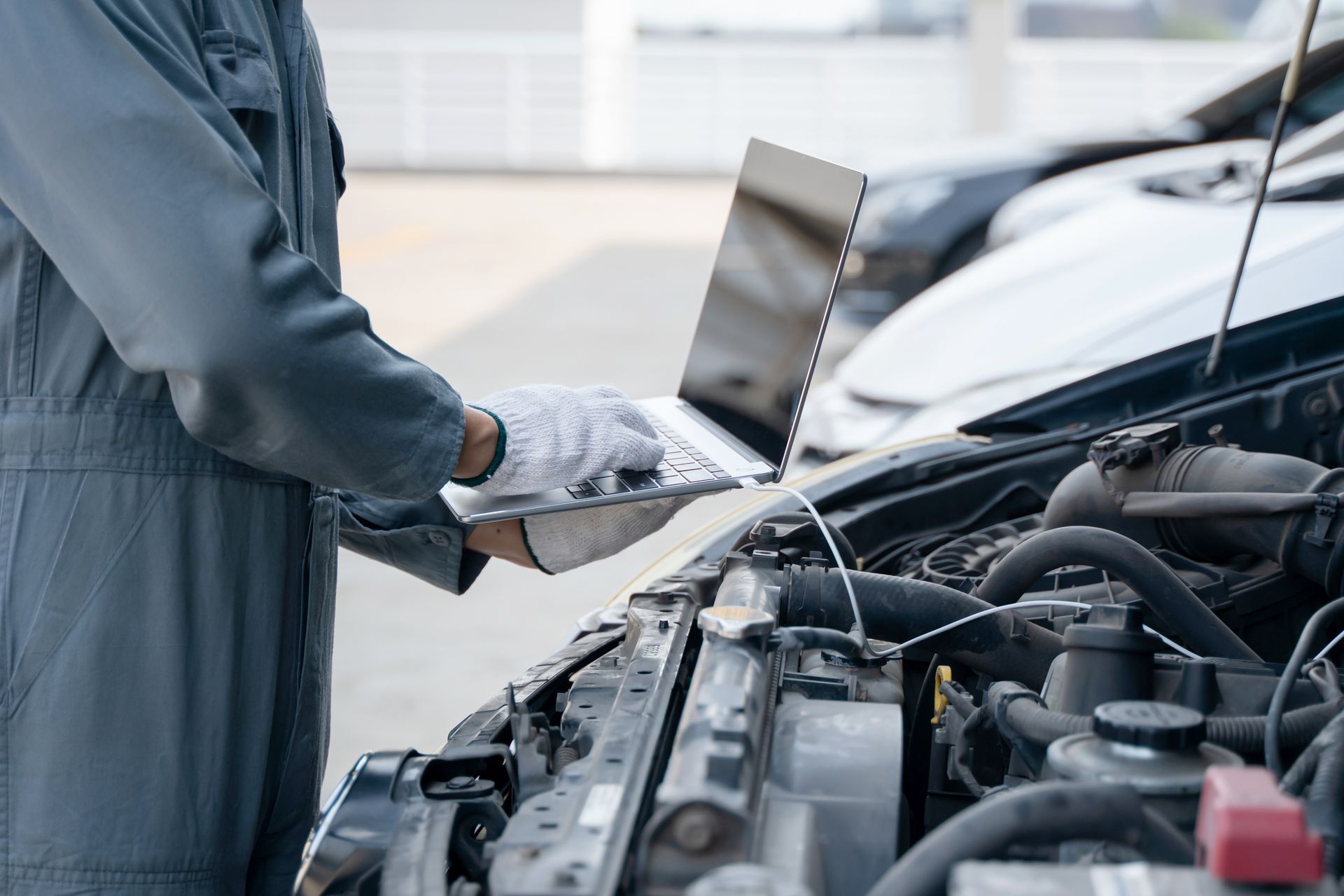 Mechanic using laptop for car diagnostics in auto workshop, modern vehicle maintenance service.