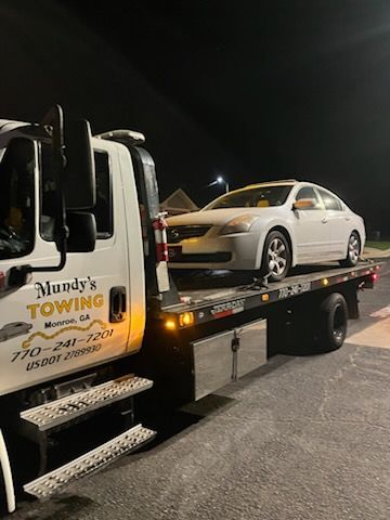 A white car is being towed by a towing truck.