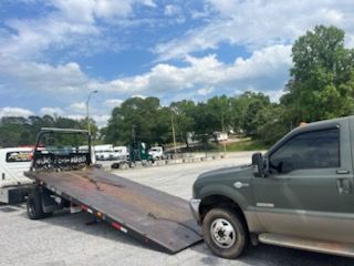 A tow truck with a flat bed is parked in a parking lot.