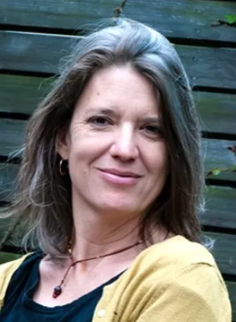 A woman wearing a yellow cardigan and a necklace smiles for the camera