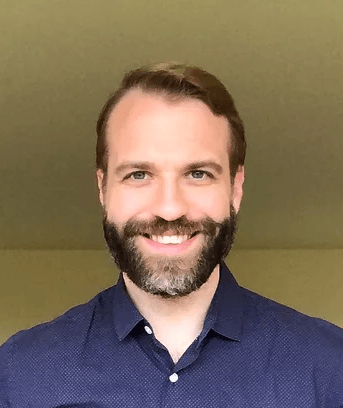 A man with a beard is smiling for the camera while wearing a blue shirt.