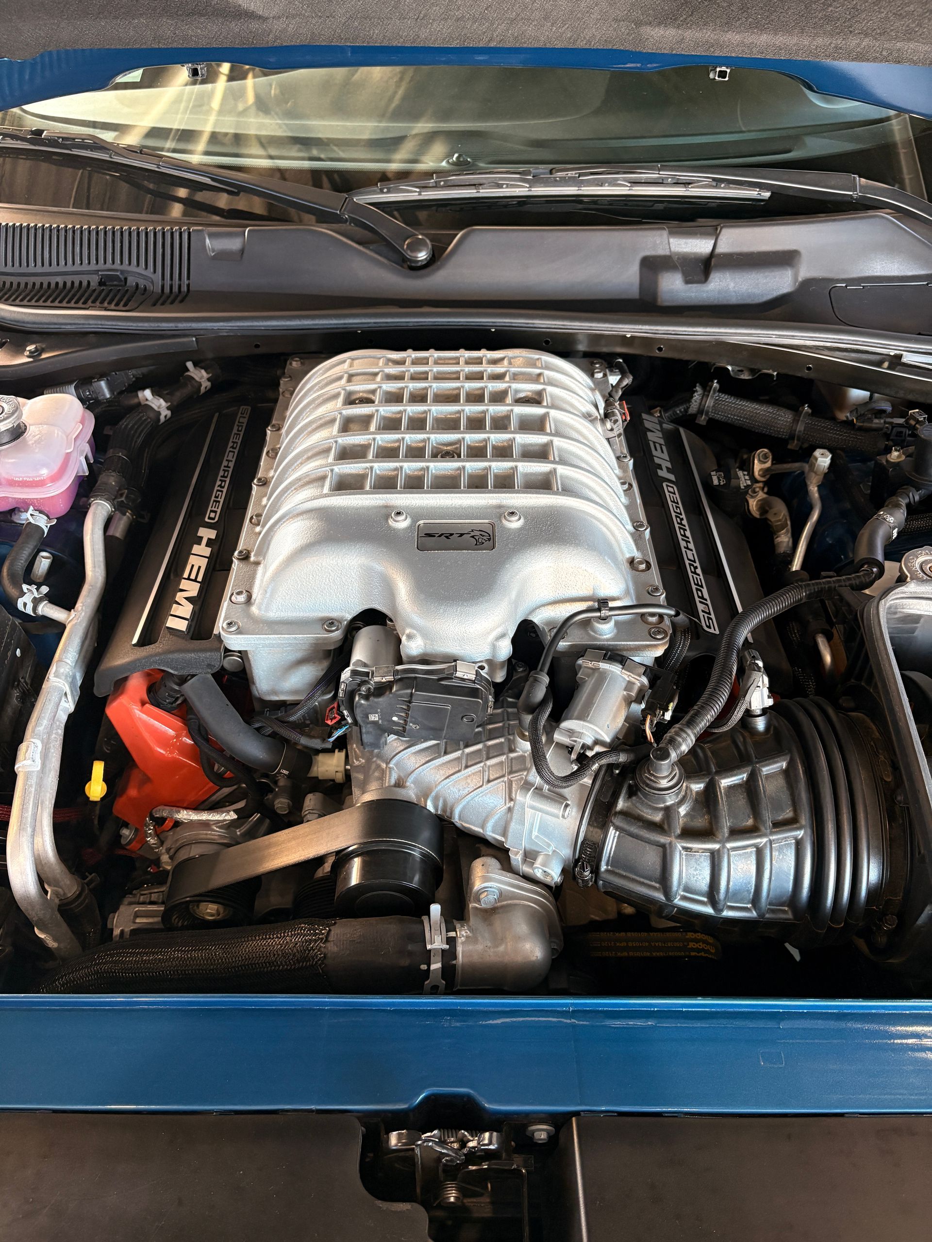 Close-up of a car engine bay with a large silver supercharger and black hoses.