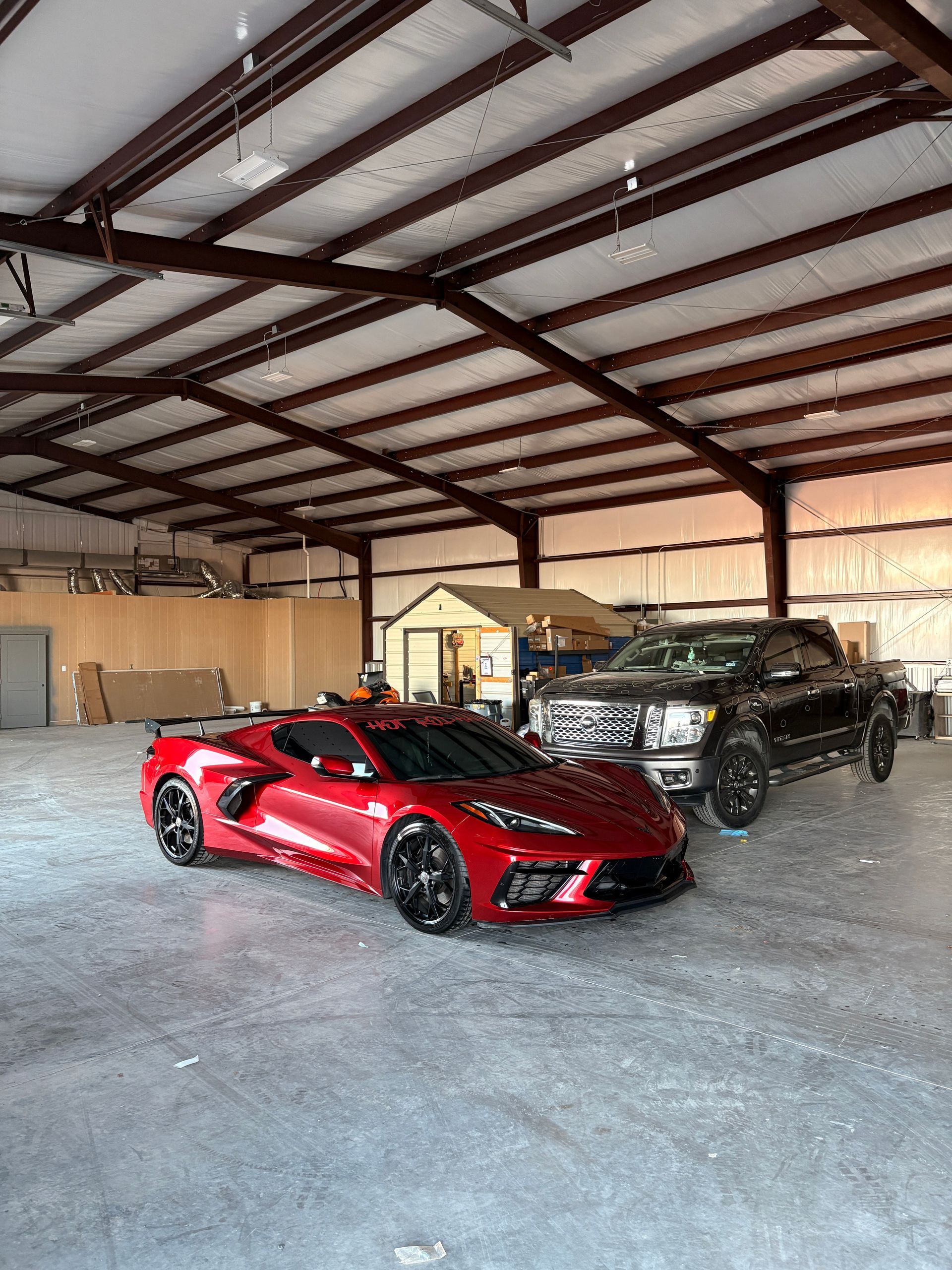 Red sports car and black SUV parked inside a large metal garage.
