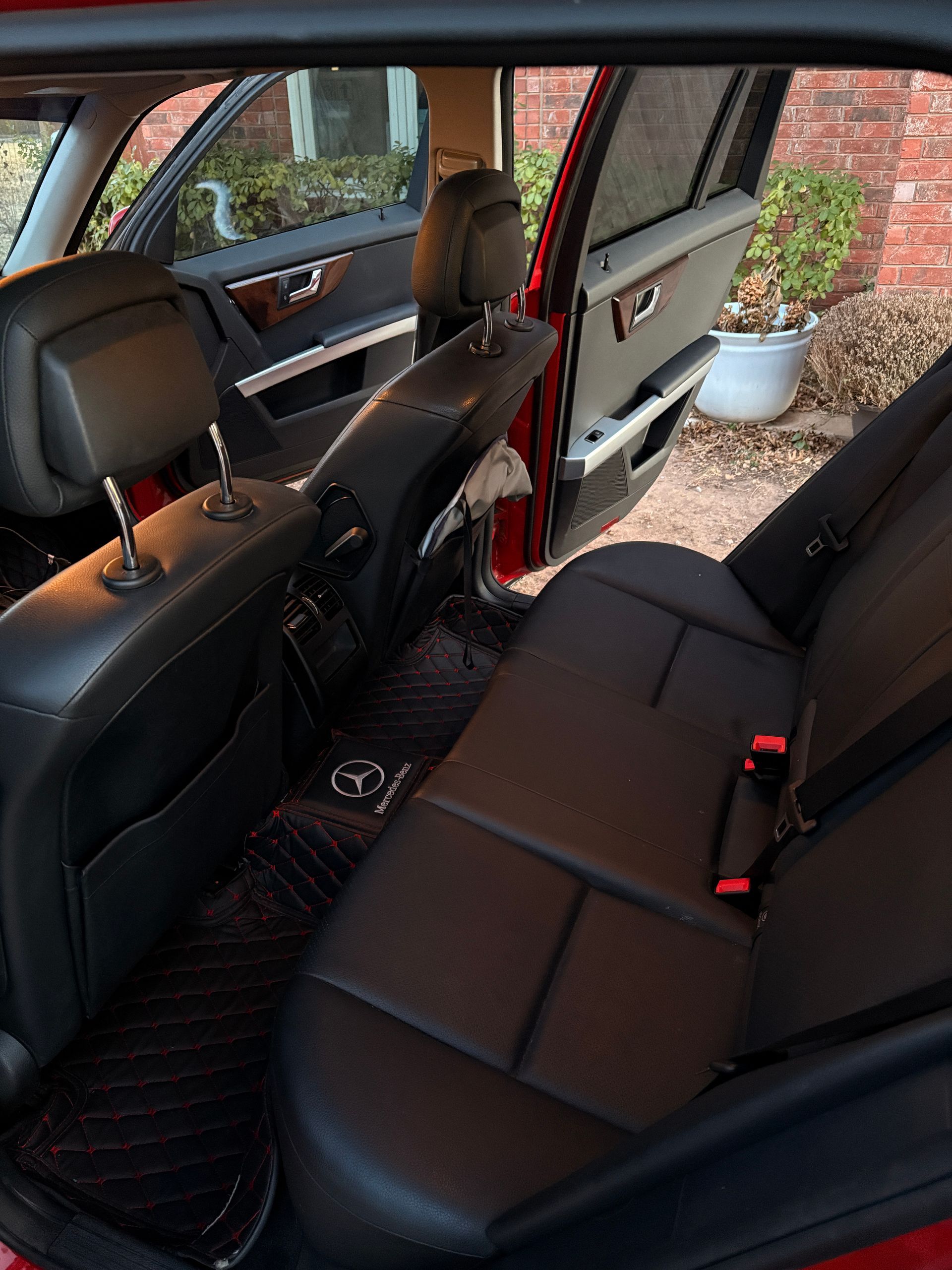 Car interior with black leather back seat, front seat back, and open rear door near a patio