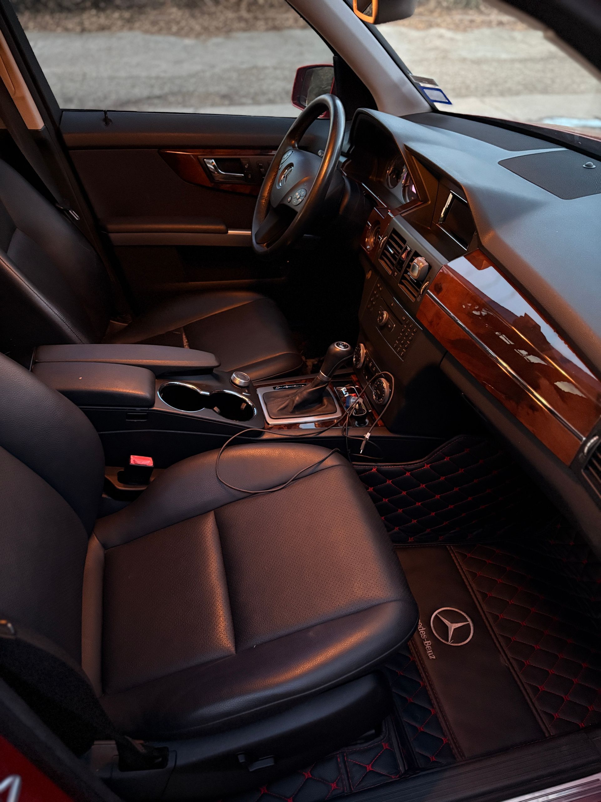 Luxury car interior with black leather seats, wood trim, and a Mercedes emblem on the floor mat.