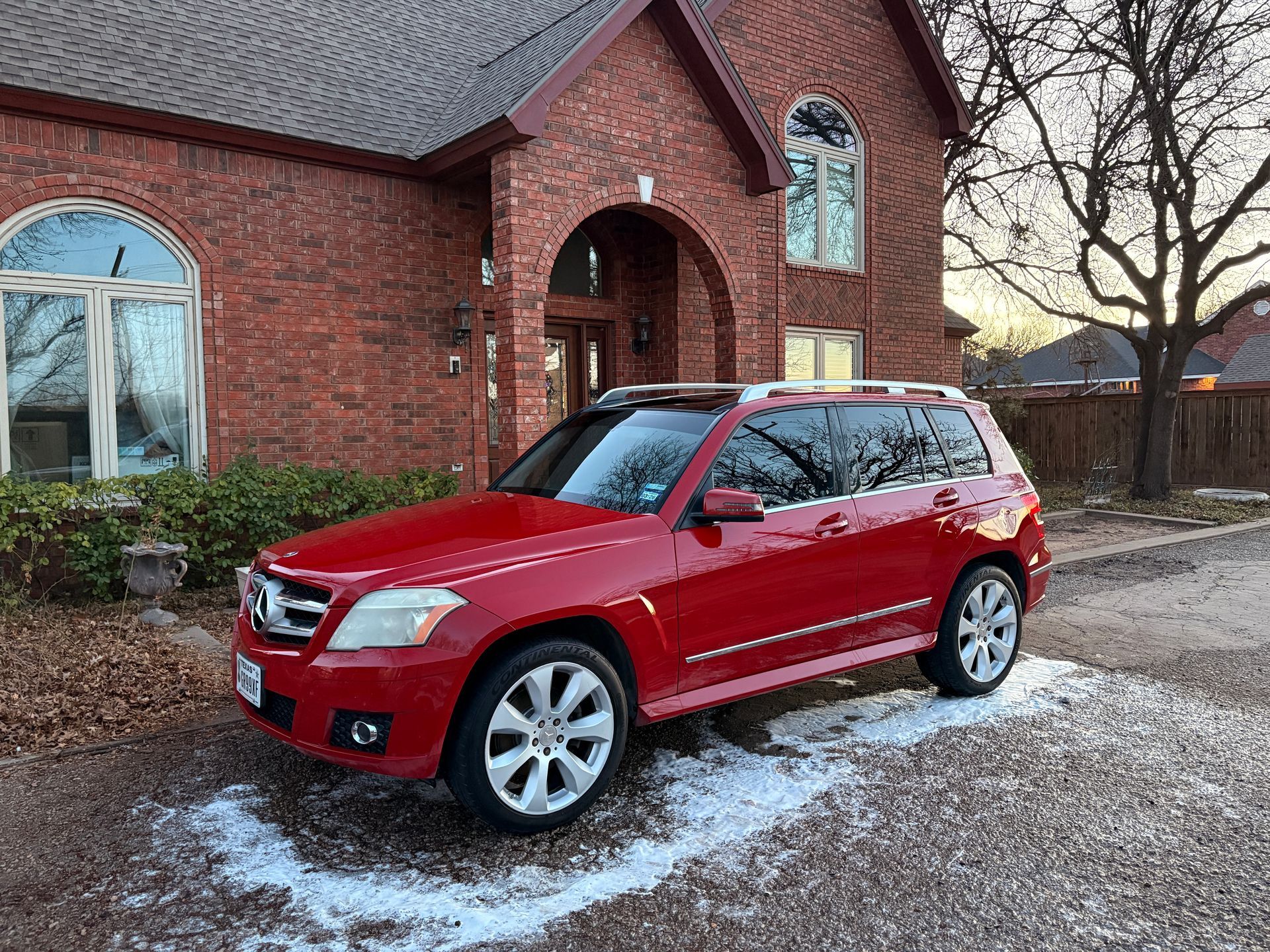 Red SUV parked outside a brick house on a snowy driveway