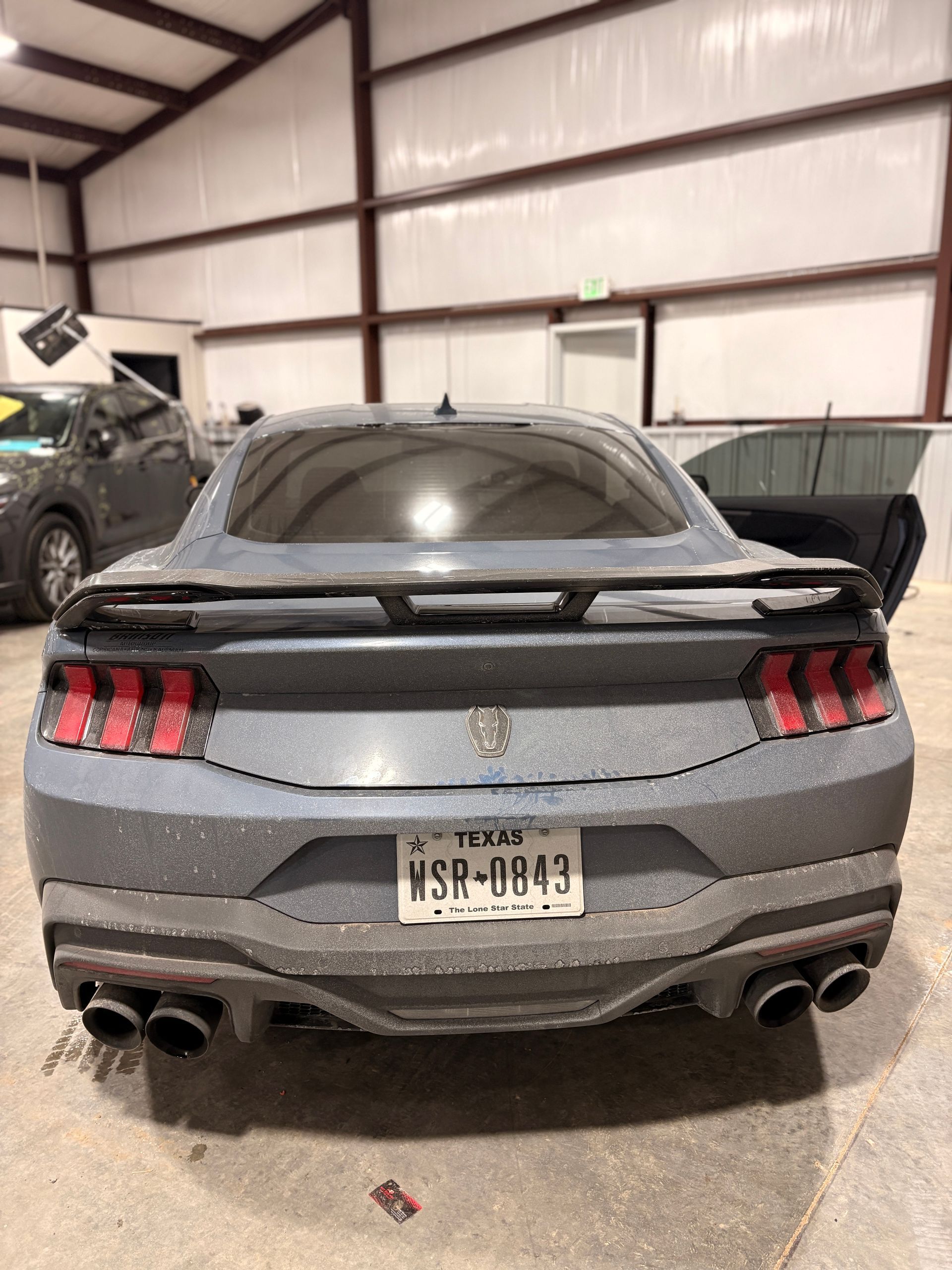 Rear view of a gray sports coupe with quad exhausts parked inside a warehouse.