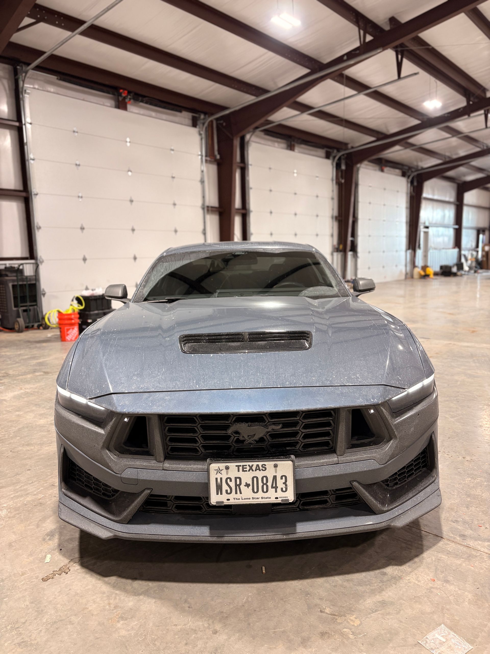 Gray sports car with front-end damage parked inside an auto repair garage