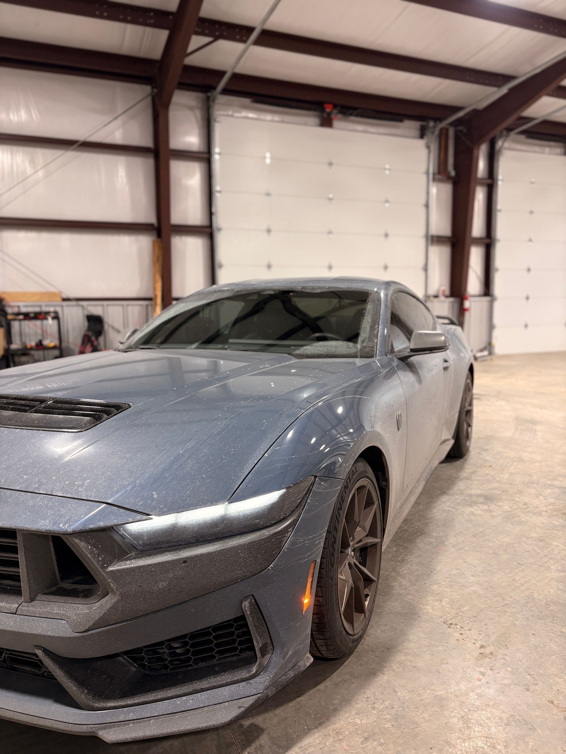 Gray sports car inside a garage, covered in water droplets