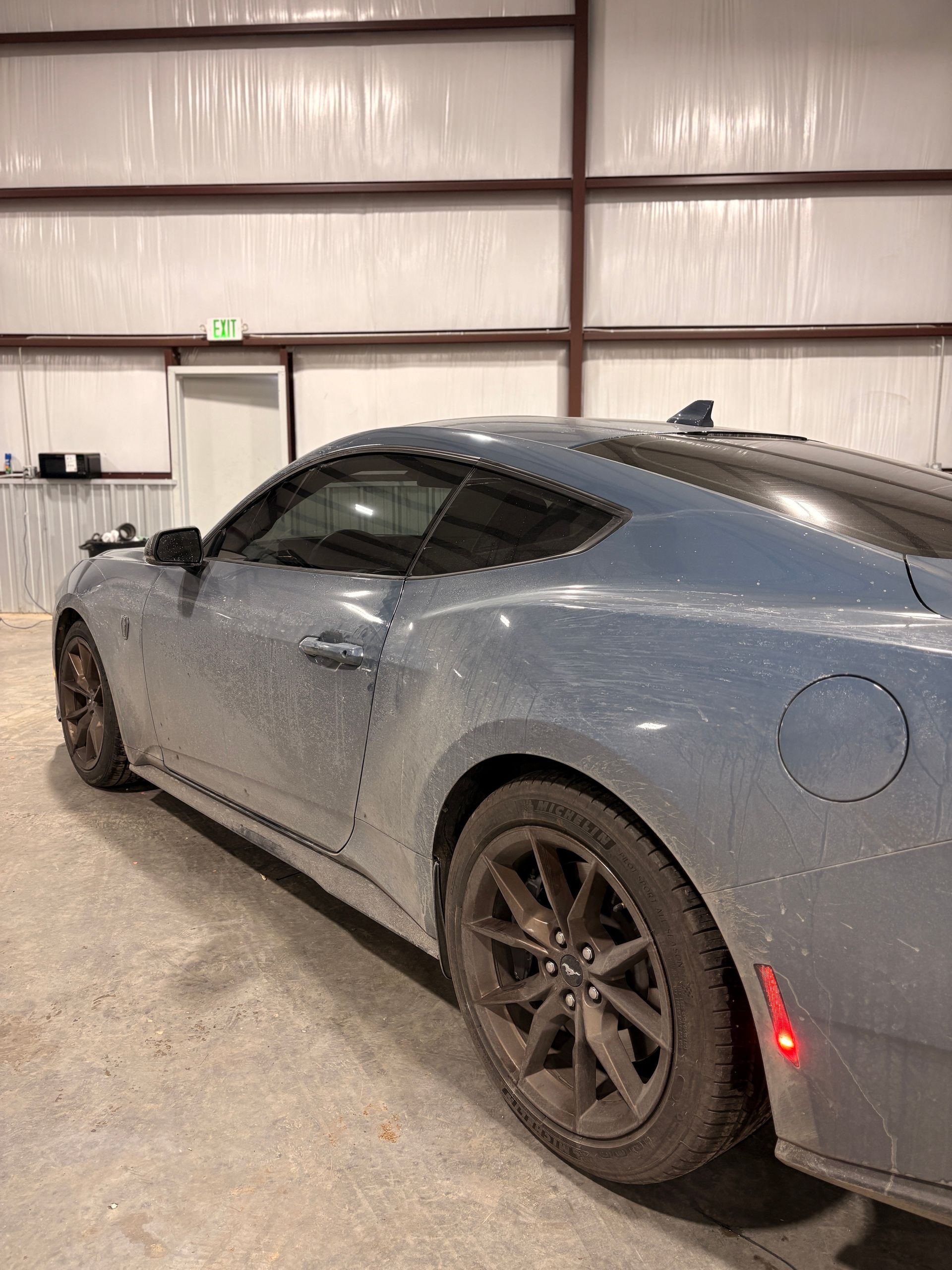 Gray sports coupe parked inside a warehouse with a concrete floor and metal walls