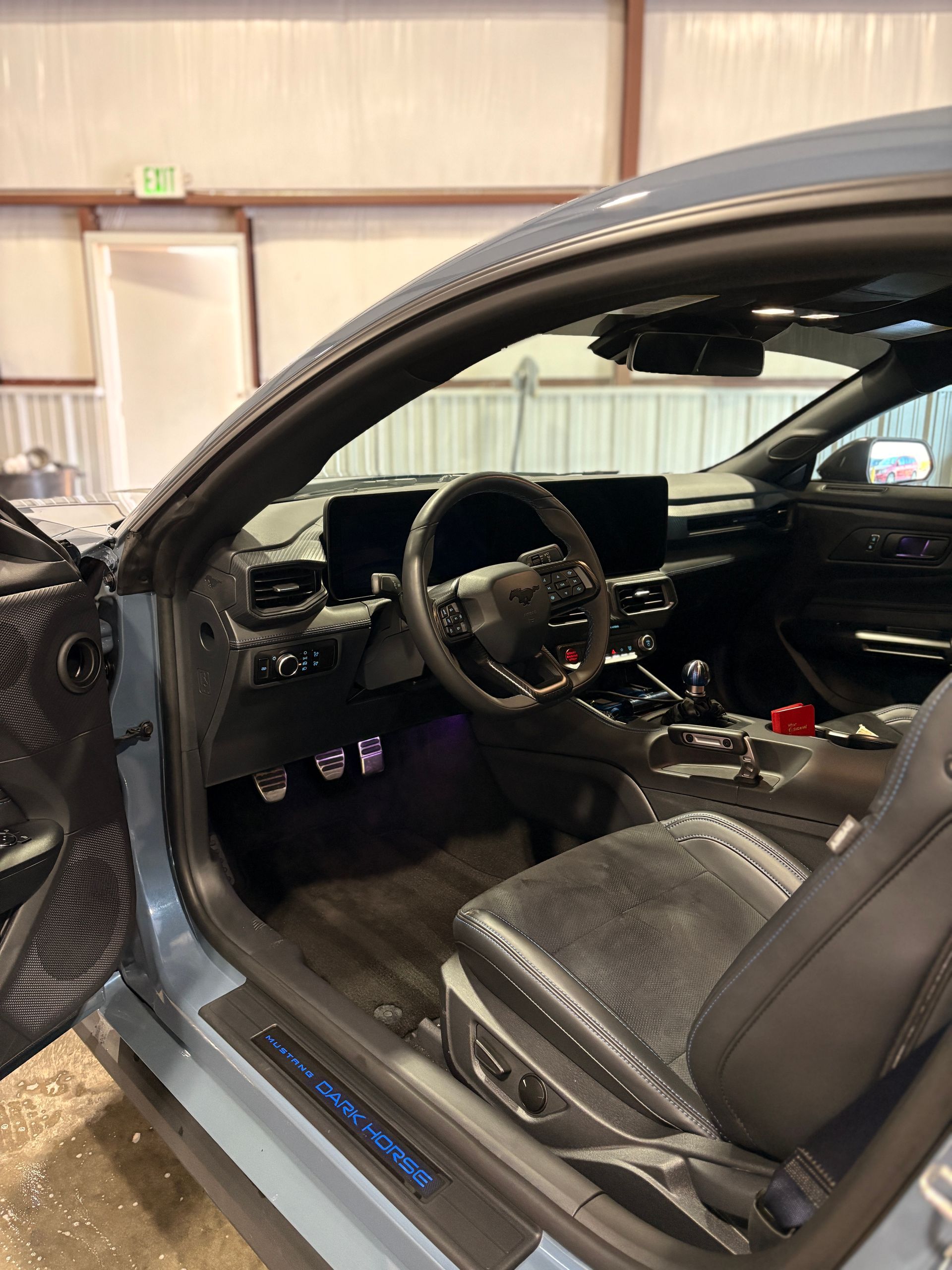 Car interior with black seats and dashboard, driver door open in a garage.