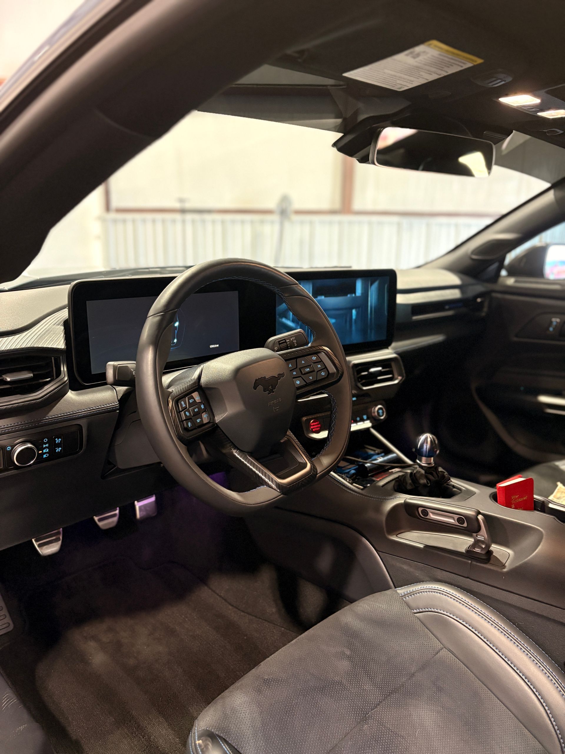 Car interior with black leather seats, digital dashboard, steering wheel, and center console in a garage.
