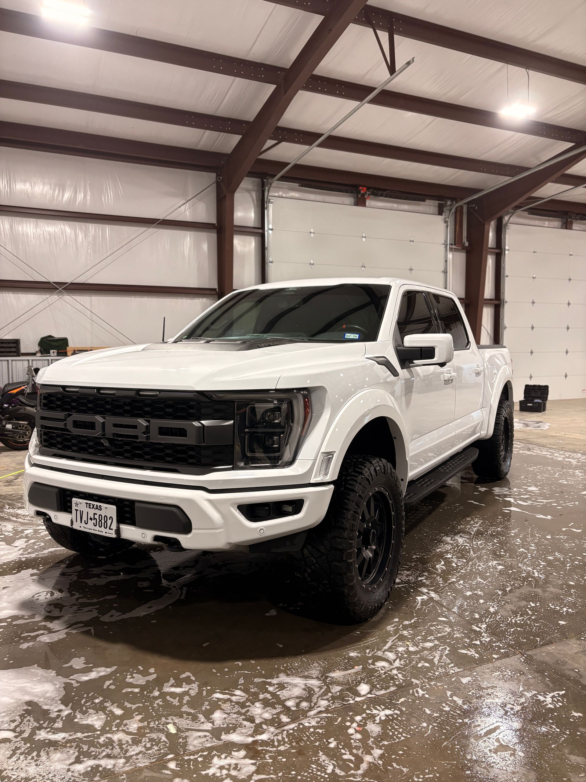 White pickup truck in a warehouse, parked on a wet floor with a metal-framed ceiling overhead