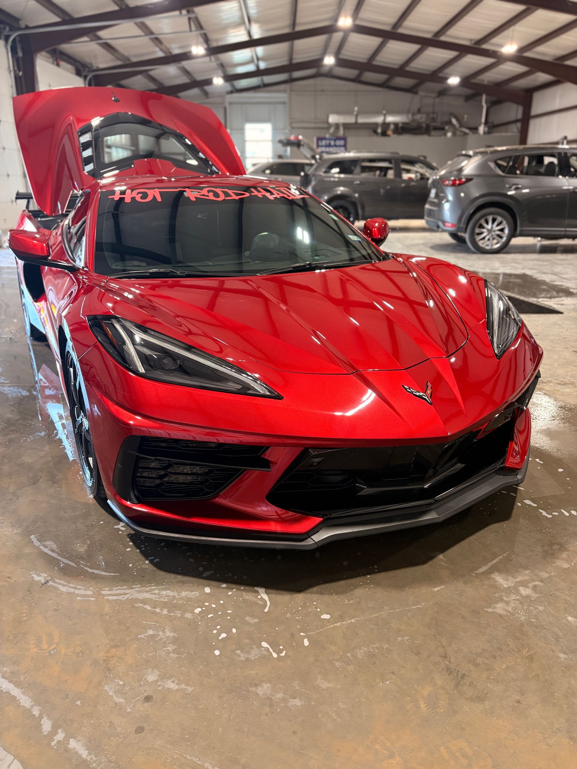 Red sports car in a garage with its hood open and front end wet from a car wash.