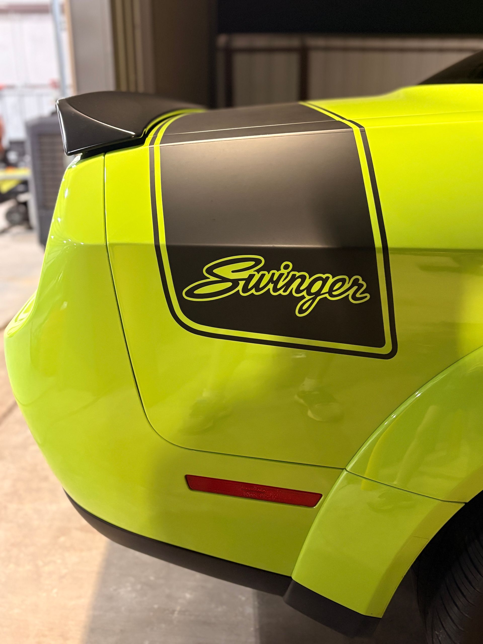 Neon yellow Swinger-branded vehicle body panel with black accents and red reflector, close-up view