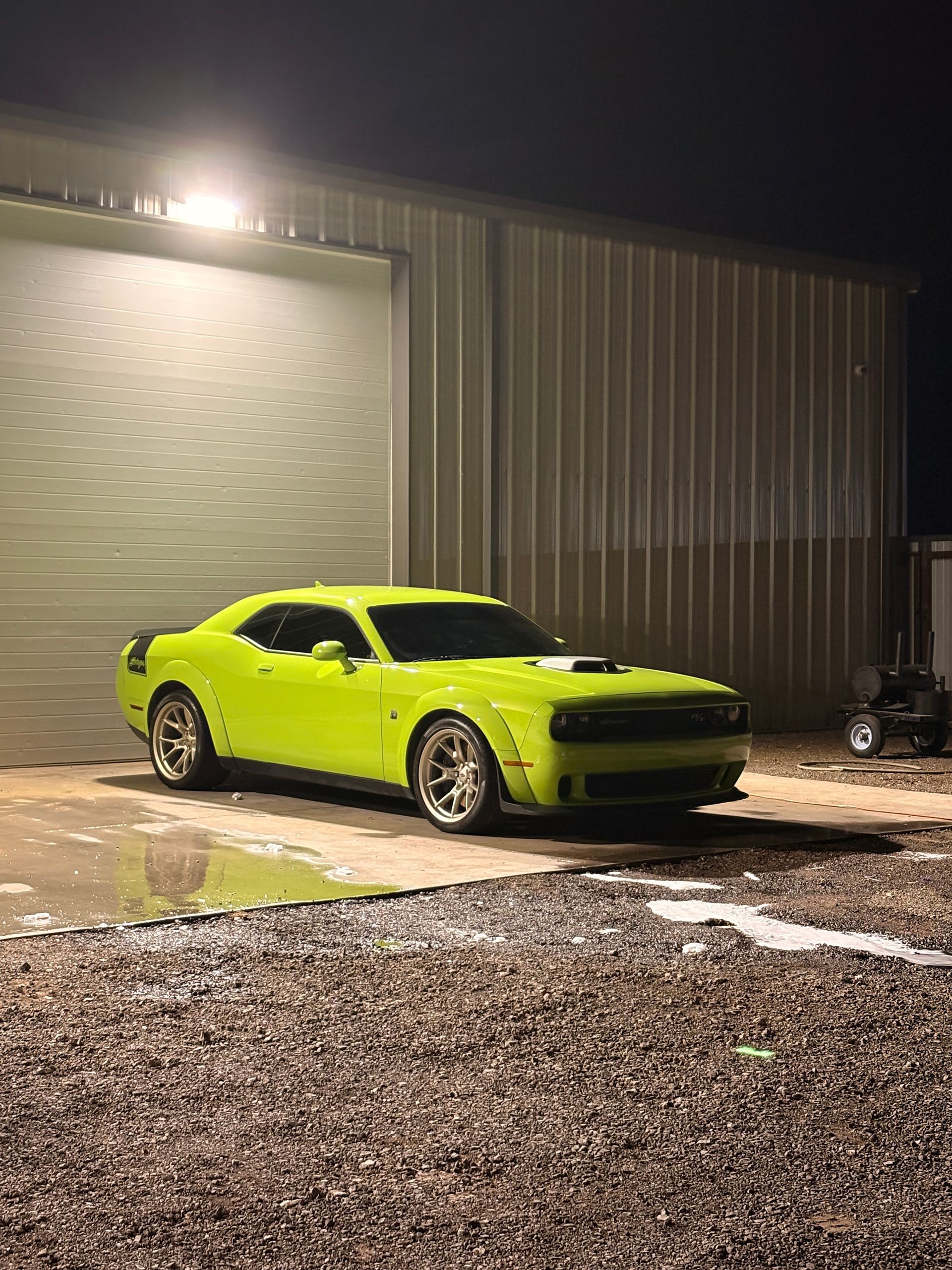 Neon green muscle car parked at night beside a metal building, lit by exterior lights.