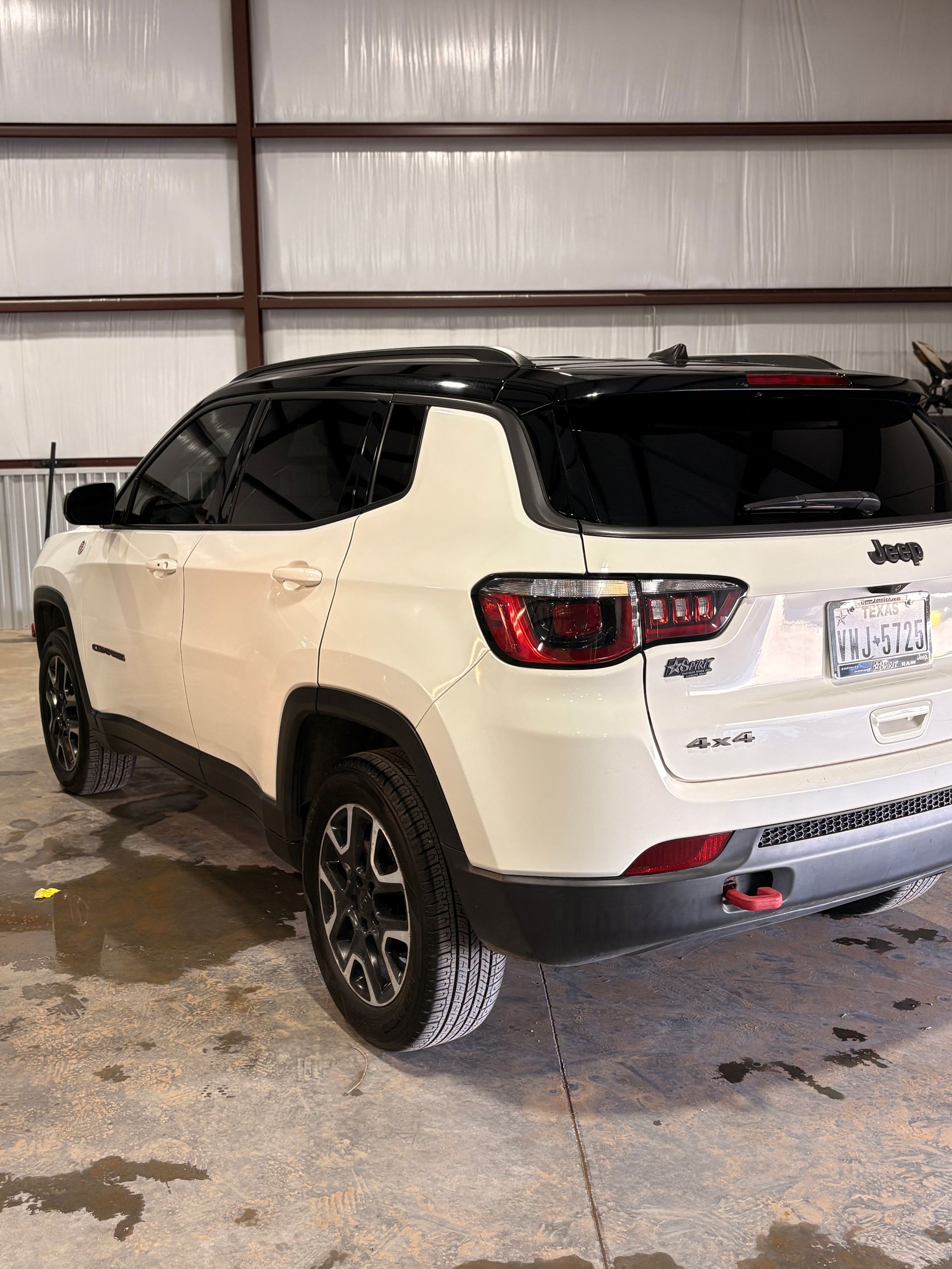 White Jeep SUV parked in a garage, rear three-quarter view, with black roof and wheels.