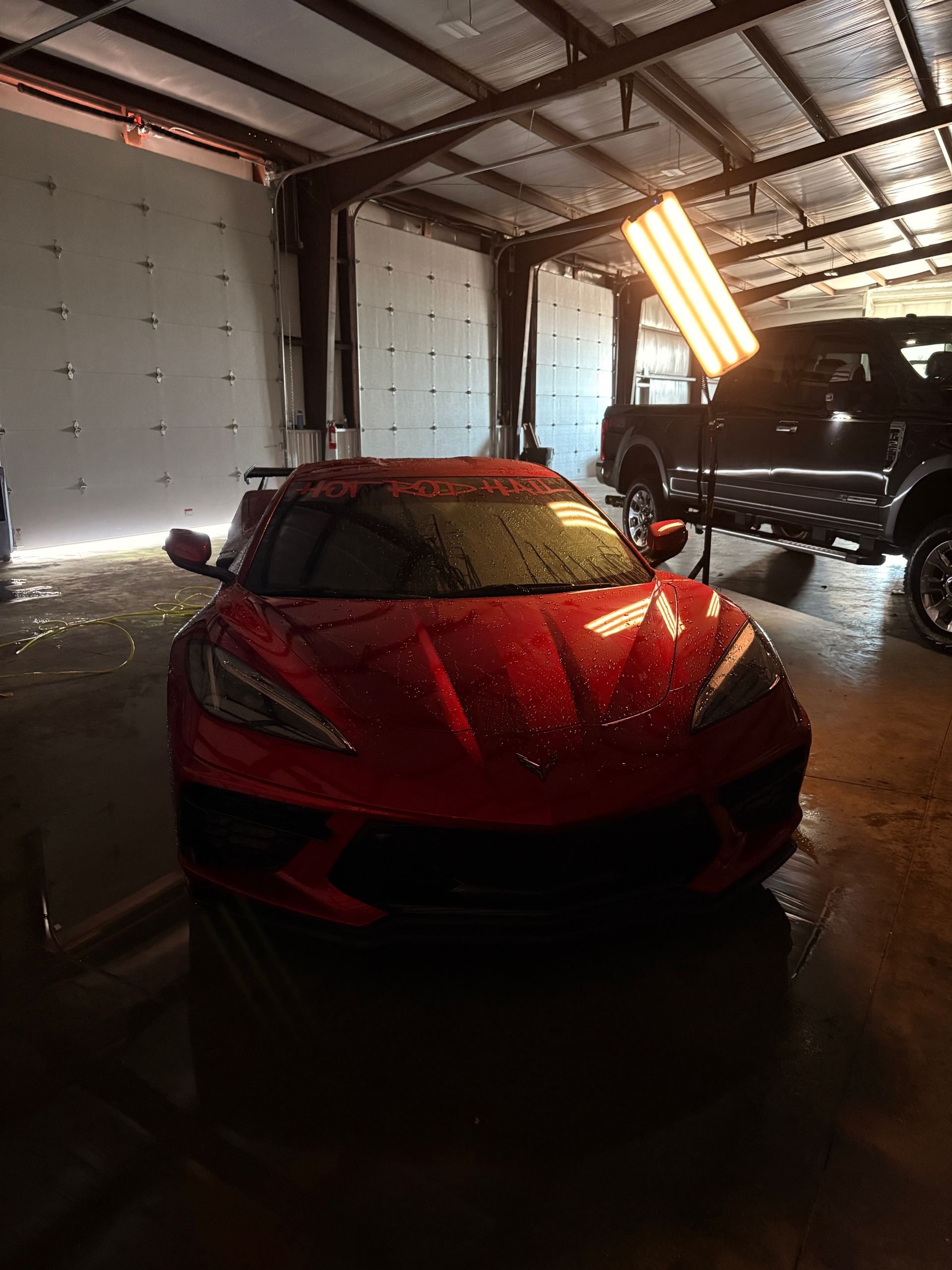Red sports car in a garage with overhead fluorescent lights and an SUV in the background