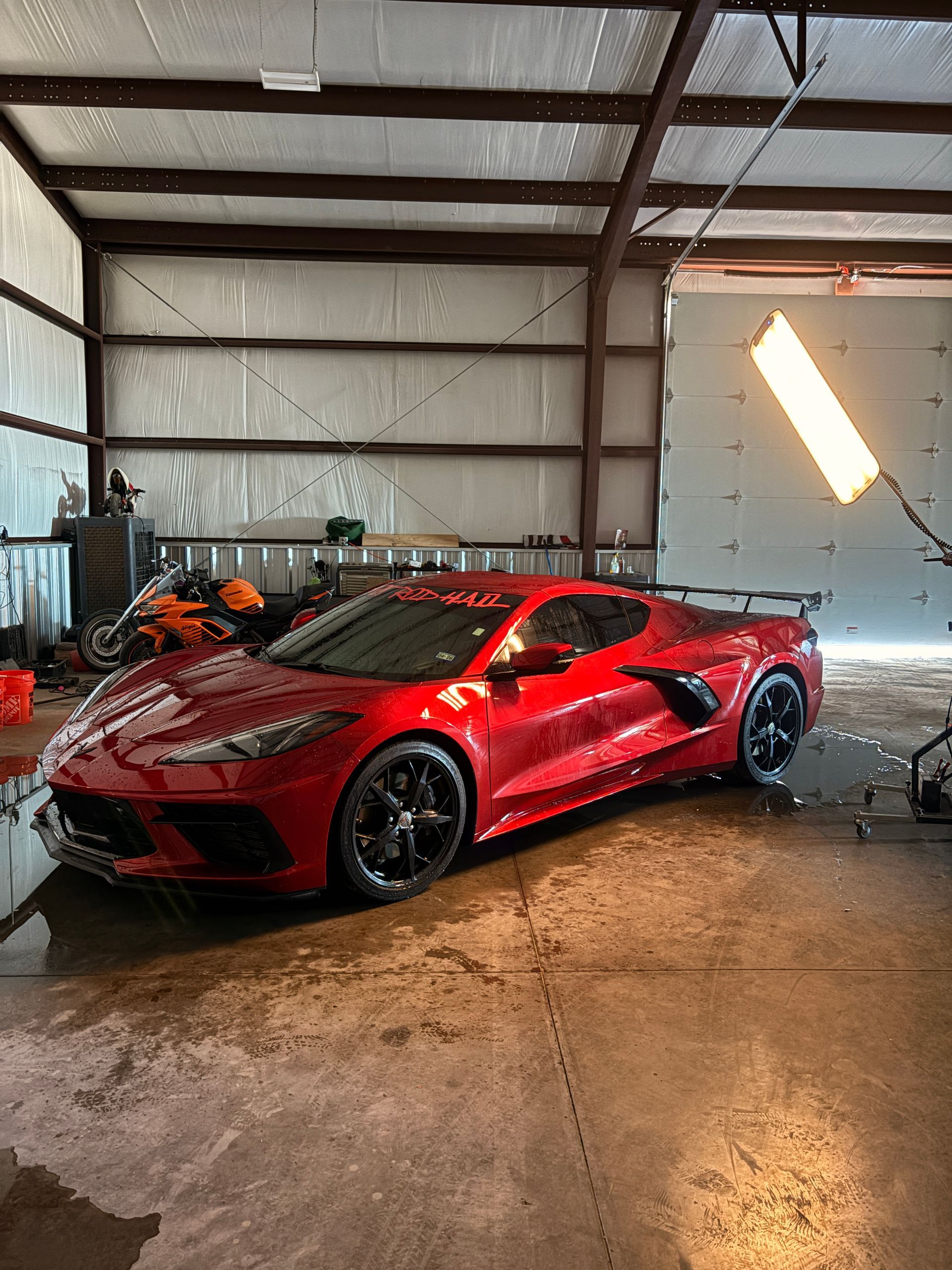 Red sports car parked inside a metal garage, with wet floor reflections and a bright door panel nearby