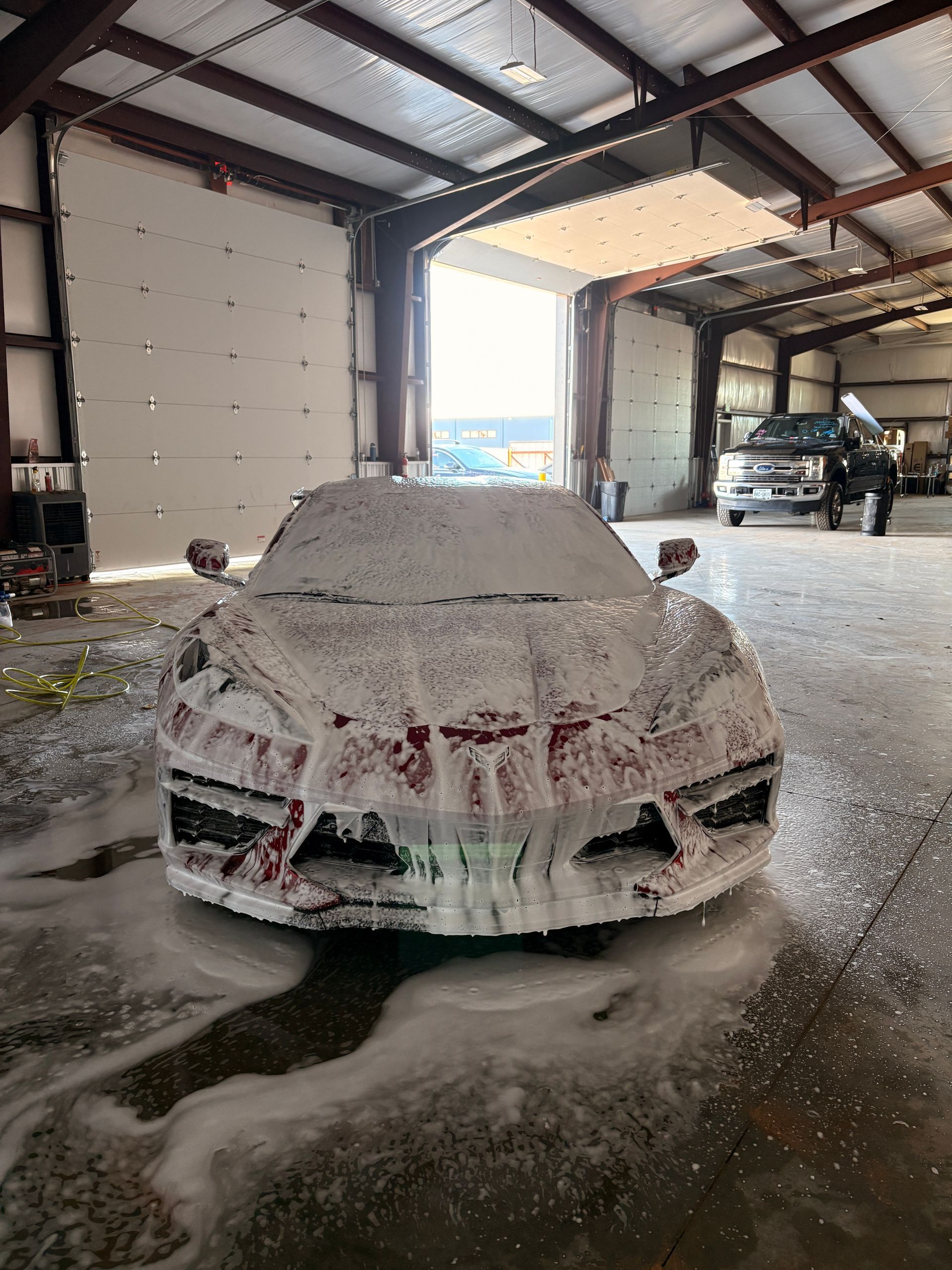 Snow-covered car in a garage, with snow piled on the hood and floor around it.